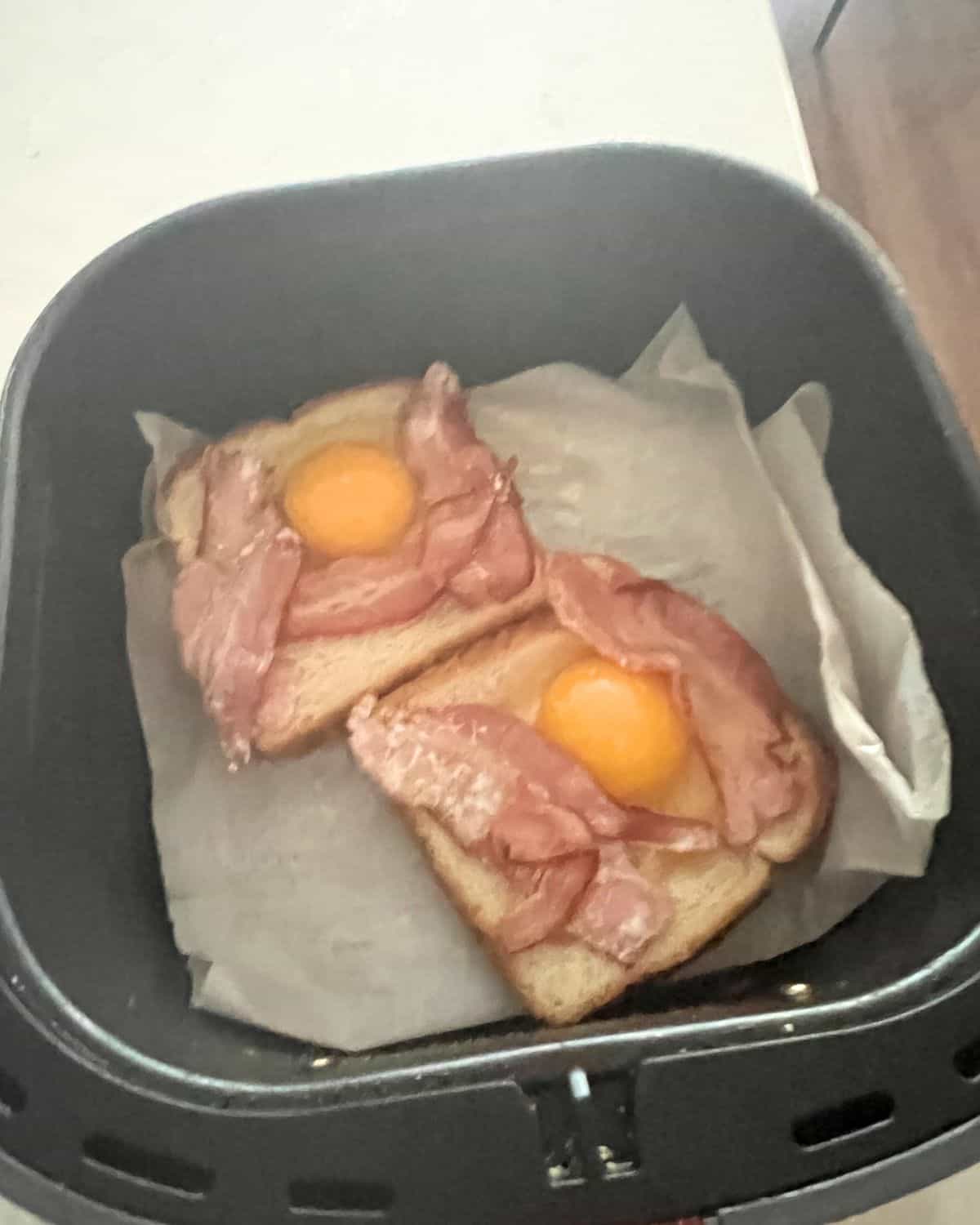 White bread with an egg and bacon on top in air fryer basket. 