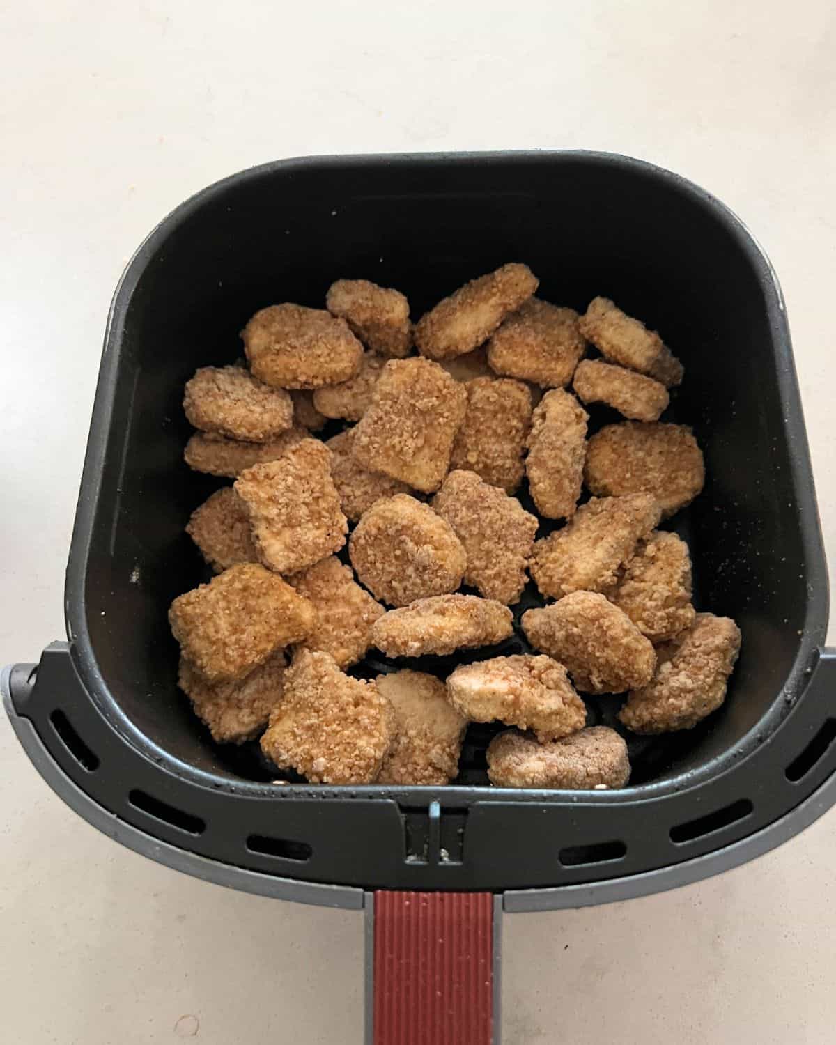 Frozen chicken nuggets in air fryer basket. 