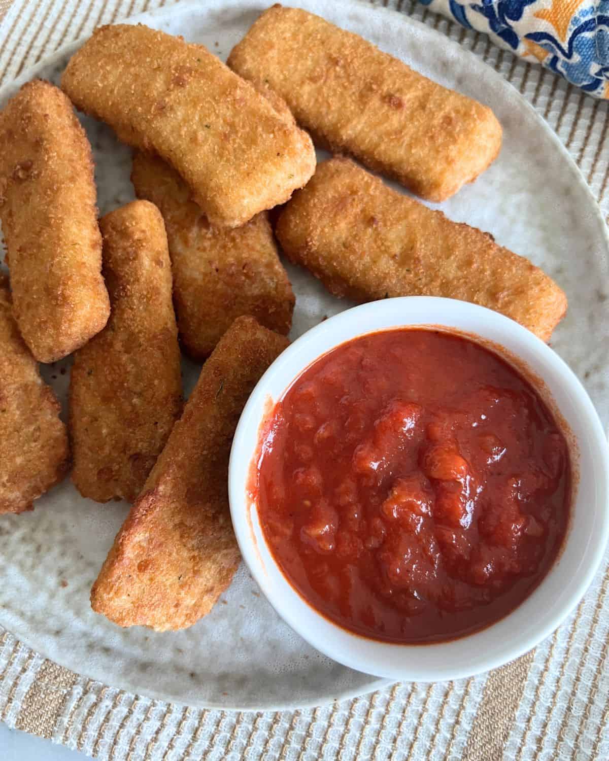 Air fried mozzarella sticks next to a side a marinara sauce on a grey plate. 