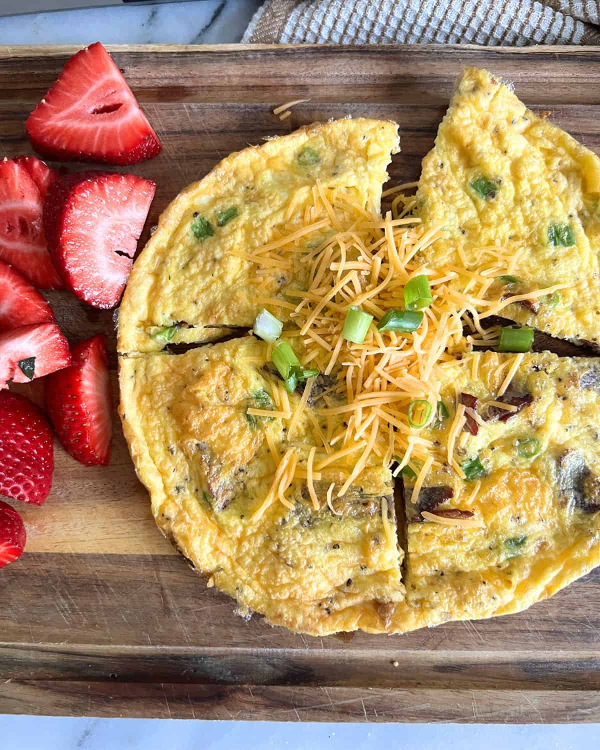 Finished air fried omelette topped with cheese and scallions next to strawberries. 
