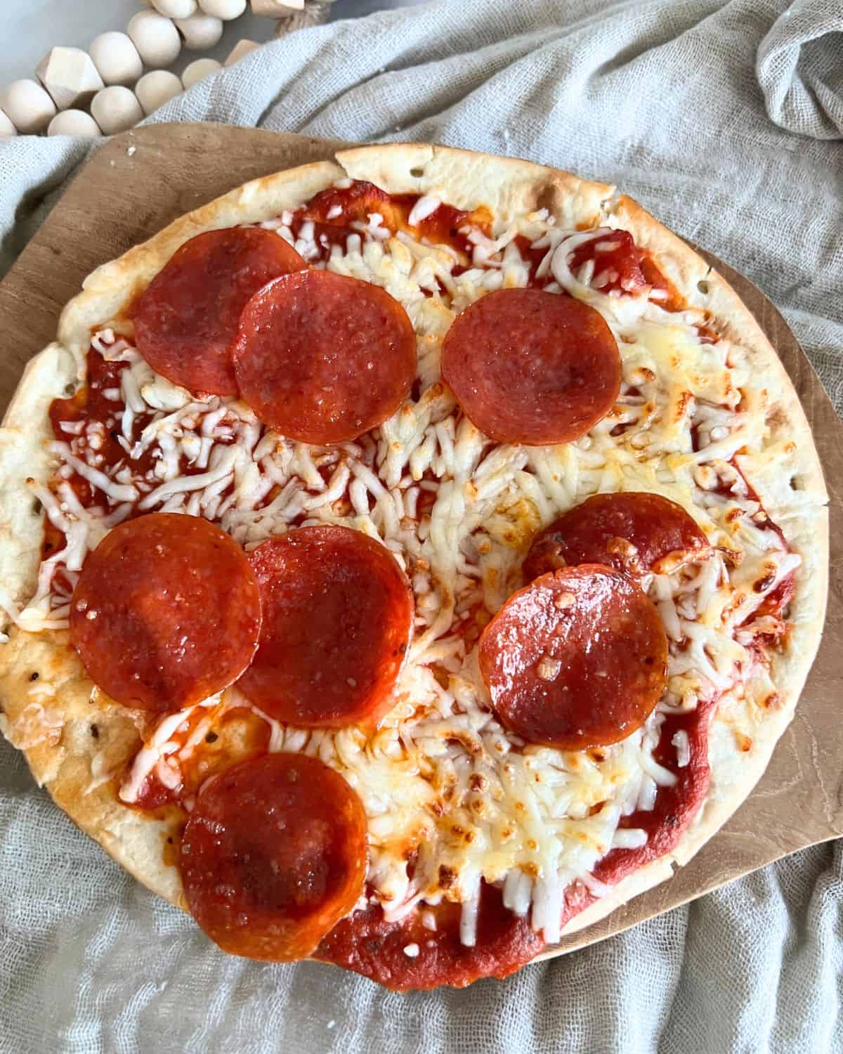 Air fryer pepperoni pita pizzas on a wooden cutting board.