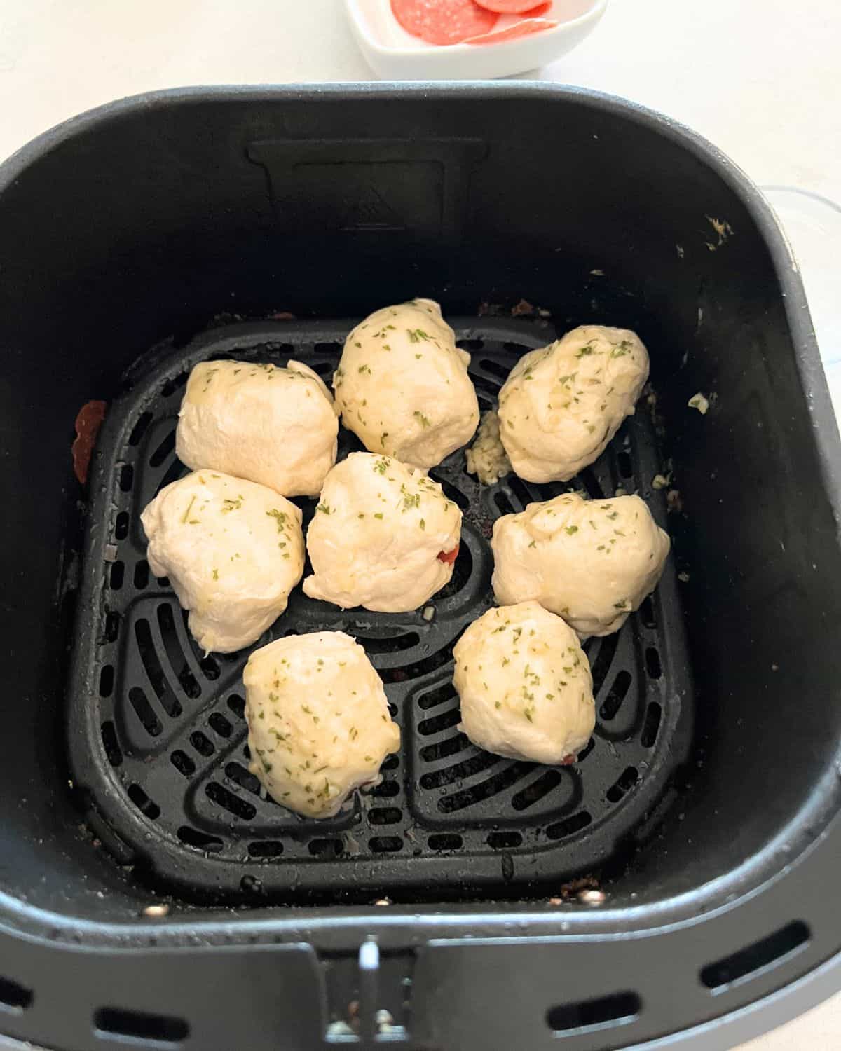Pepperoni and string cheese  rolled up into a dough balls in air fryer basket. 