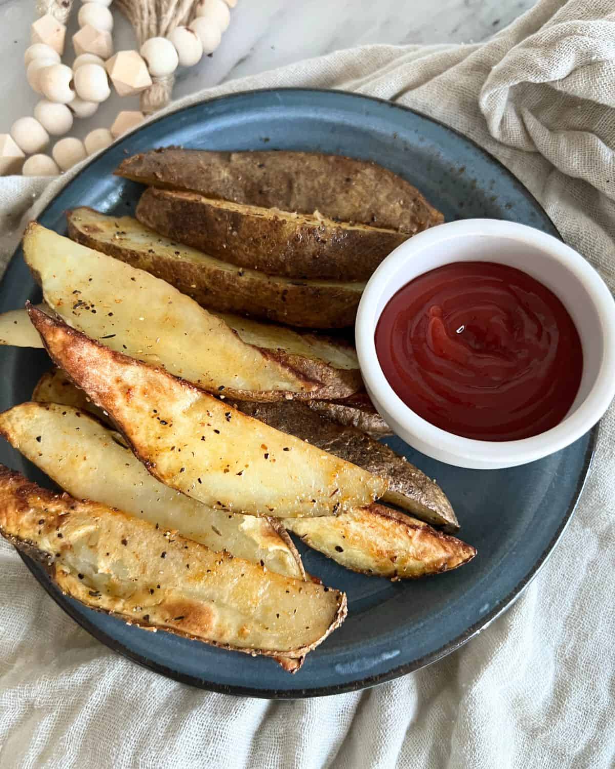 Crispy golden brown seasoned potato wedges from the air fryer next to ketchup. 
