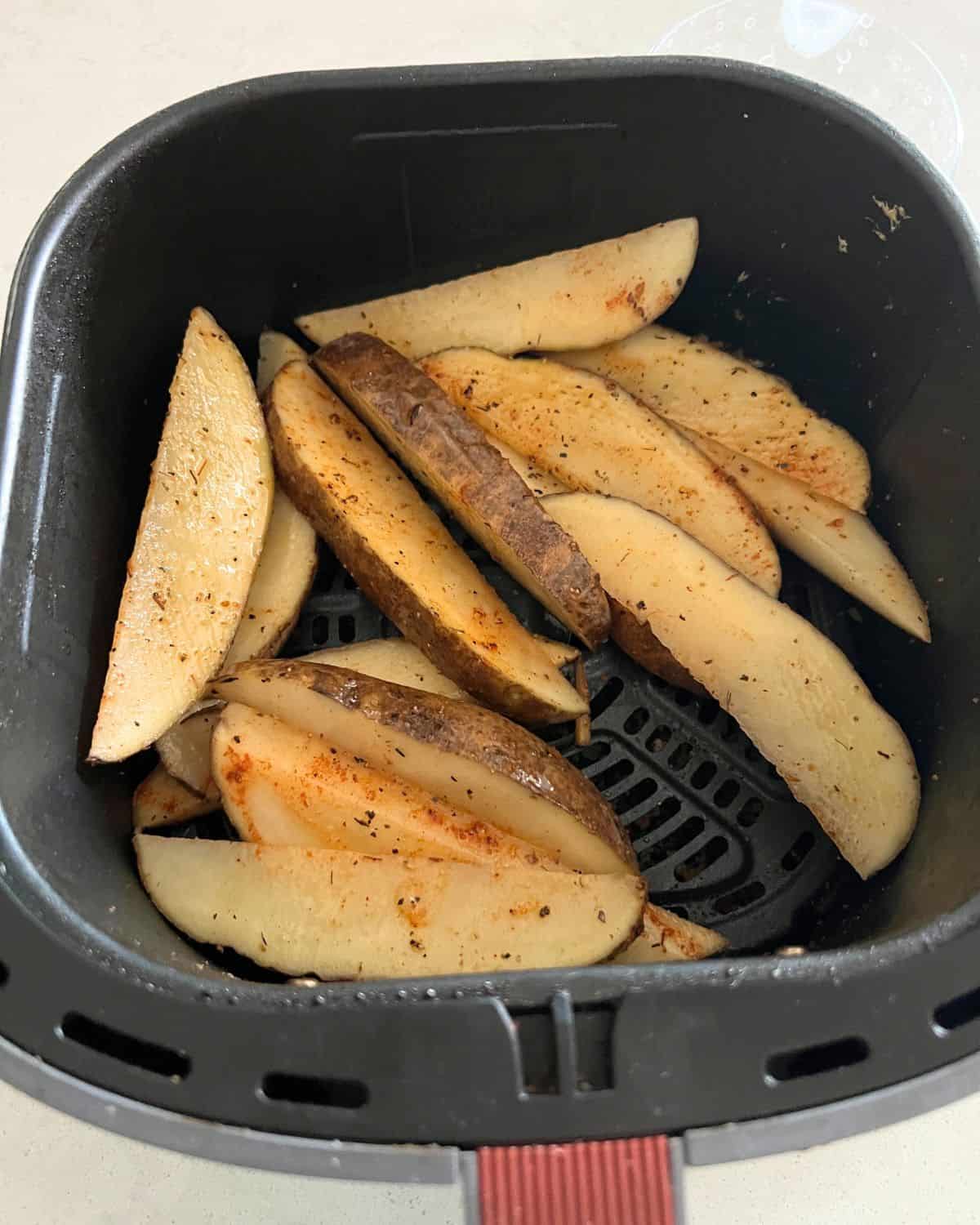 Seasoned potato wedges in air fryer basket. 