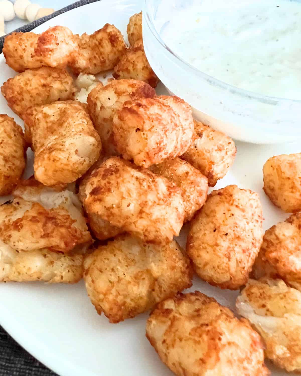 Air fryer cajun tater tots next to a bowl of sauce. 