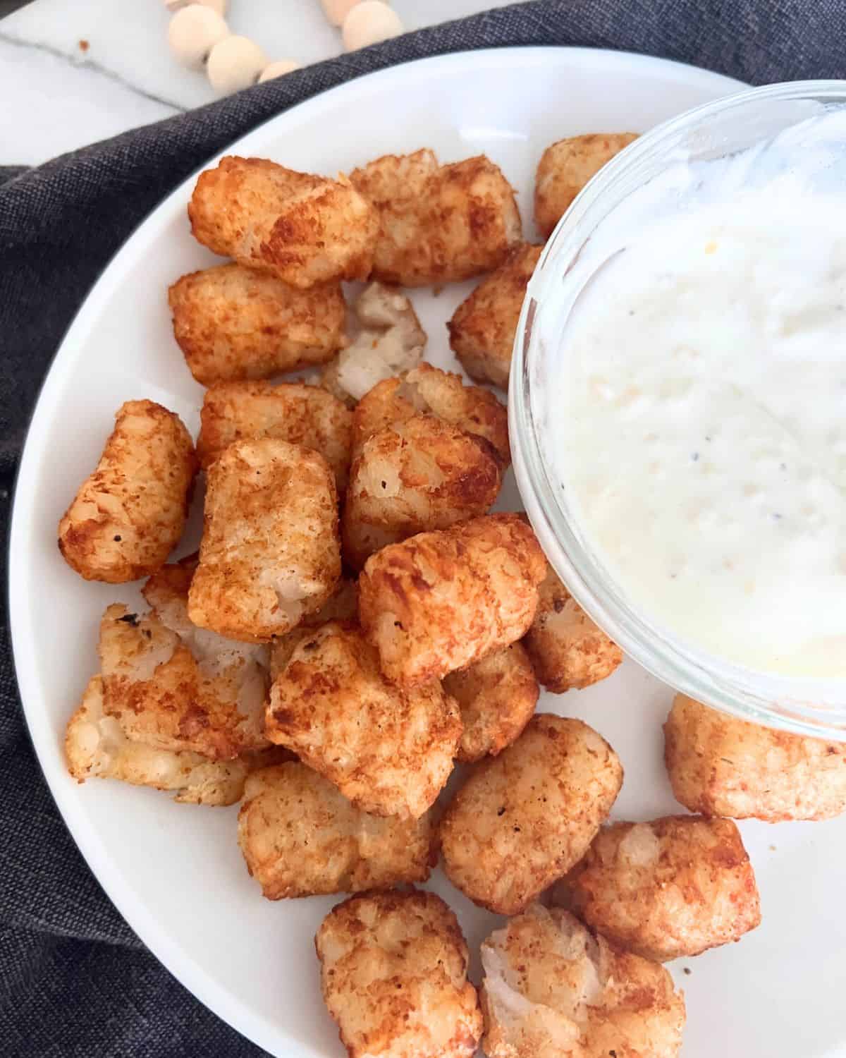 Tater tots and garlic dipping sauce served on a white plate. 