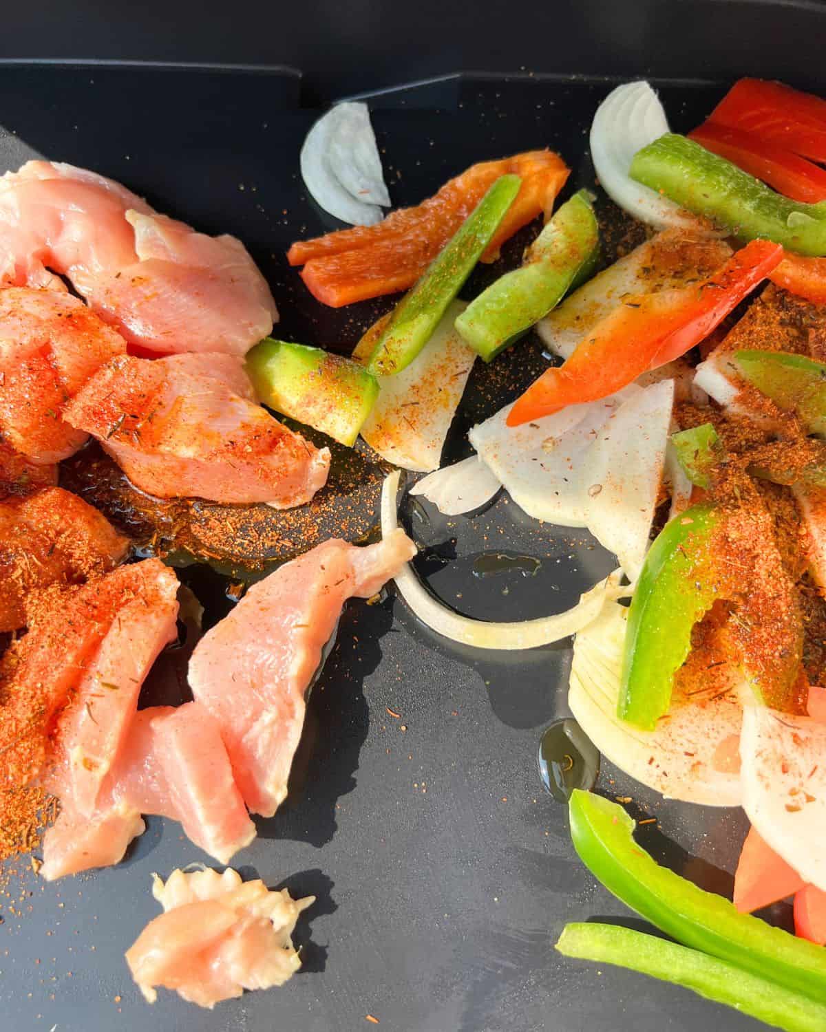 Uncooked seasoned chicken and vegetables on a griddle. 