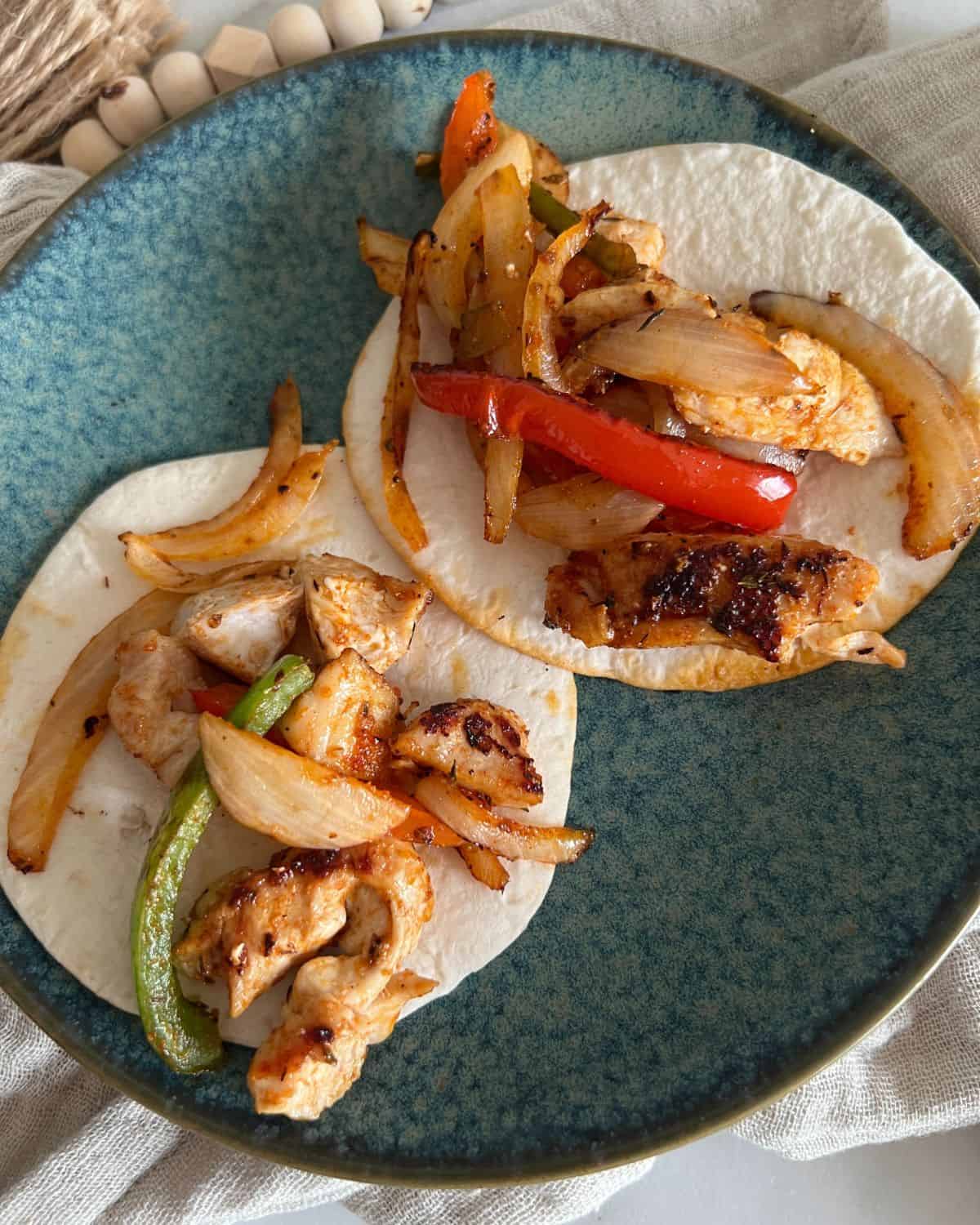 Two chicken fajitas on street style tortillas on a blue plate. 