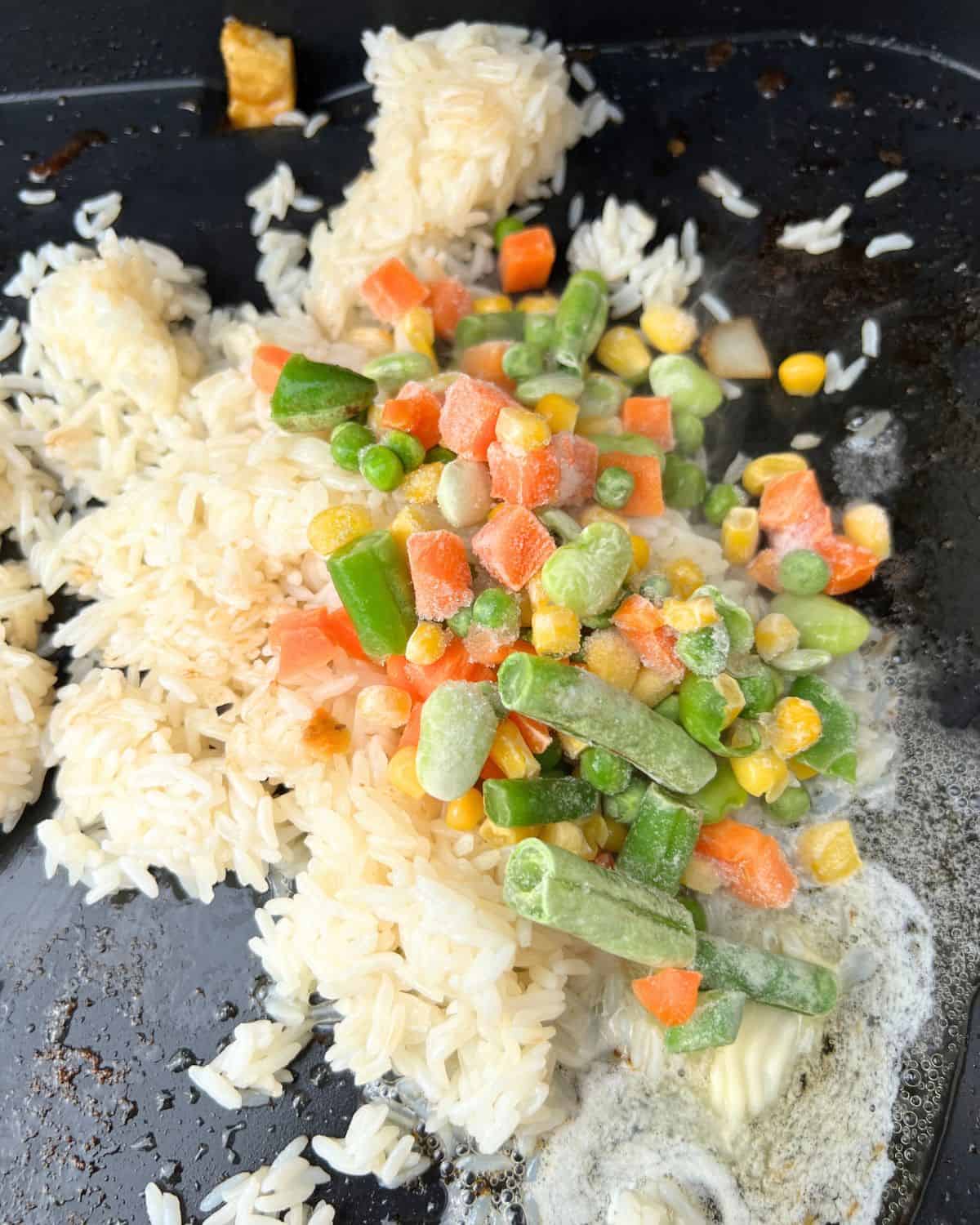 Frozen mixed vegetables cooking with rice on a Blackstone. 