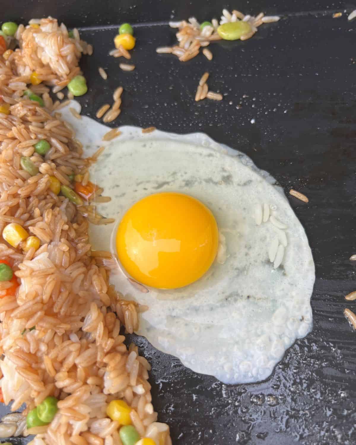 Egg cooking next to fried rice on a Blackstone. 