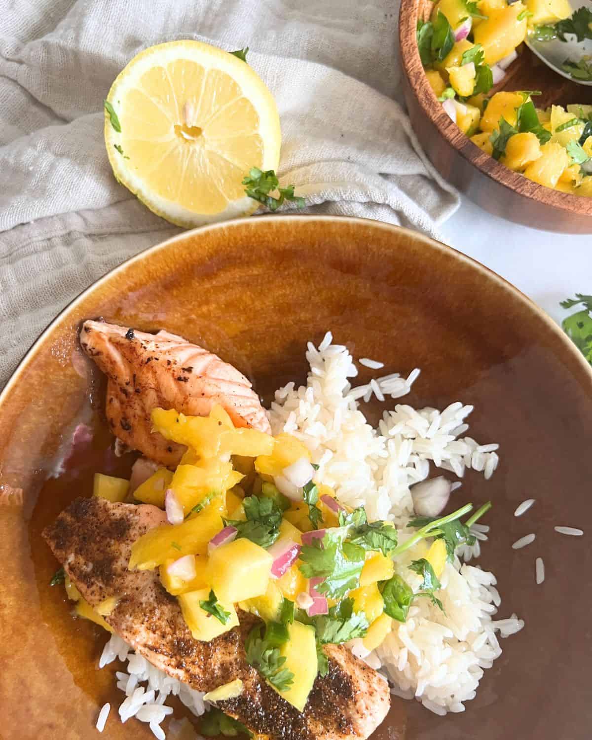 Salmon topped with mango salsa and served over rice next to a lemon. 