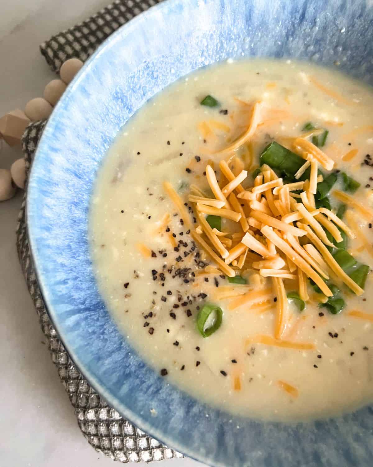 Crock pot potato soup in a blue bowl topped with cheese and green onions. 