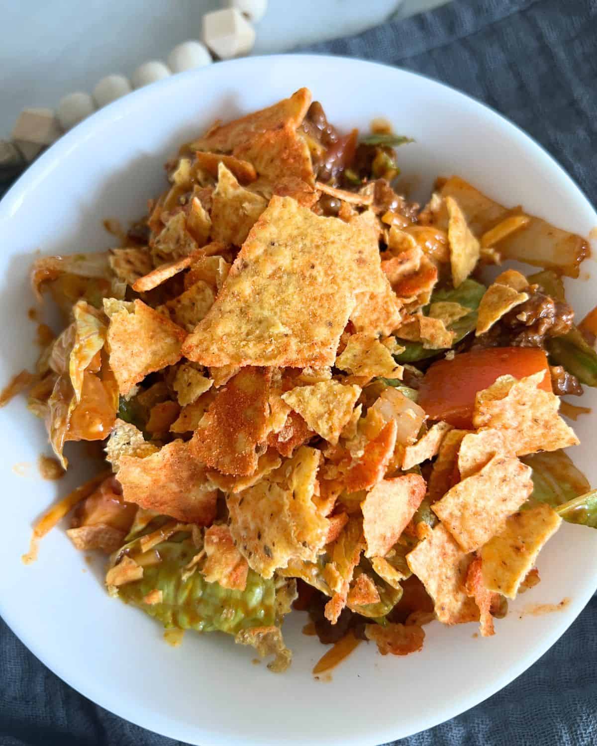 Dorito salad in a white bowl topped with cheese flavored tortilla chips and Catalina dresssng. 