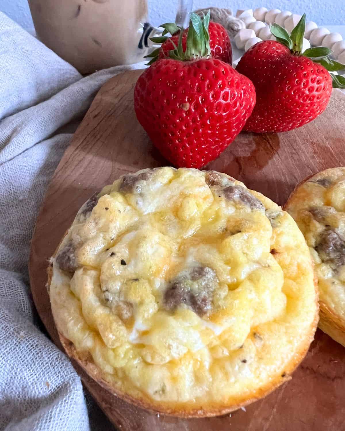 Finished egg and sausage muffins on a wood board with strawberries. 