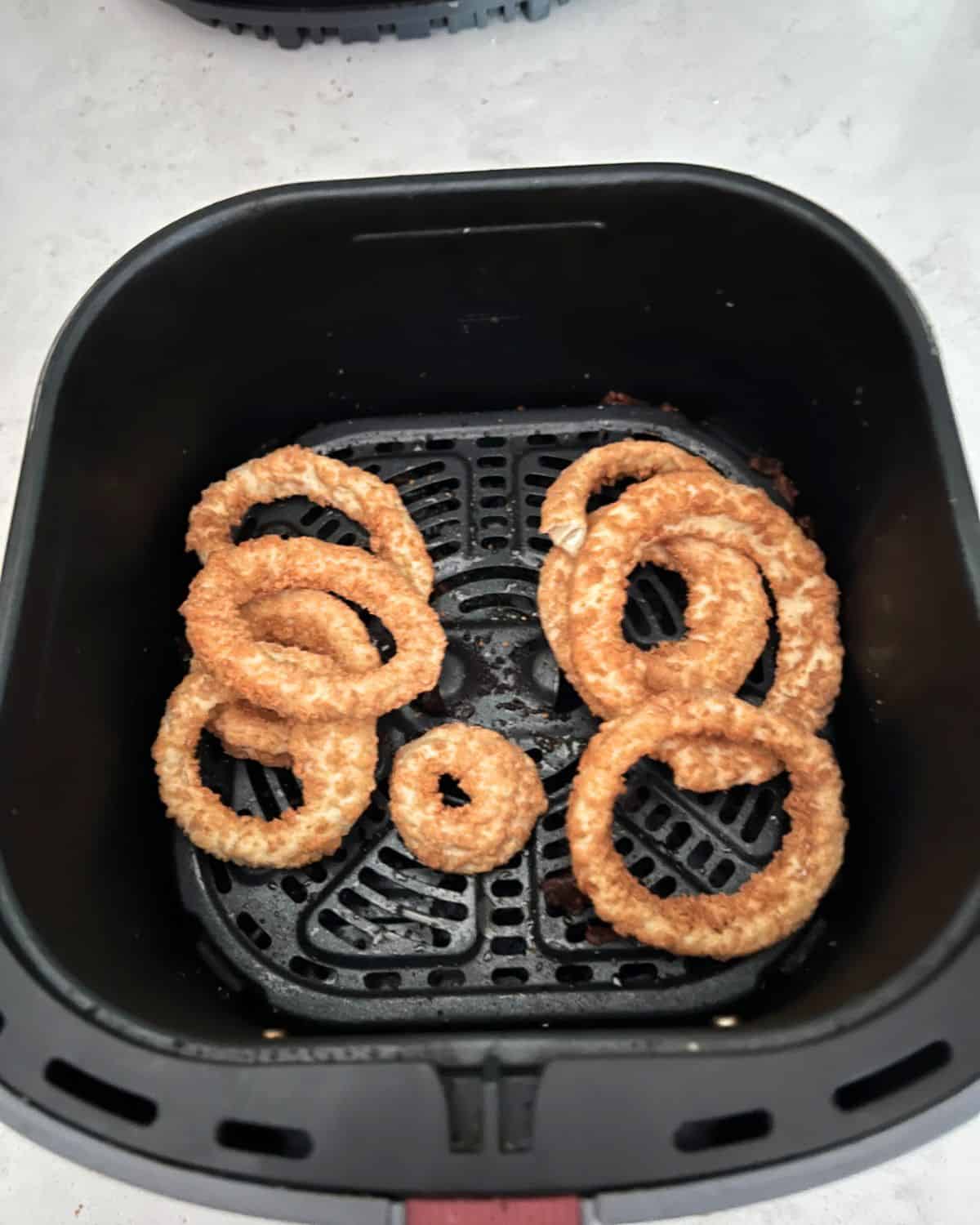 Frozen onion rings in air fryer basket. 