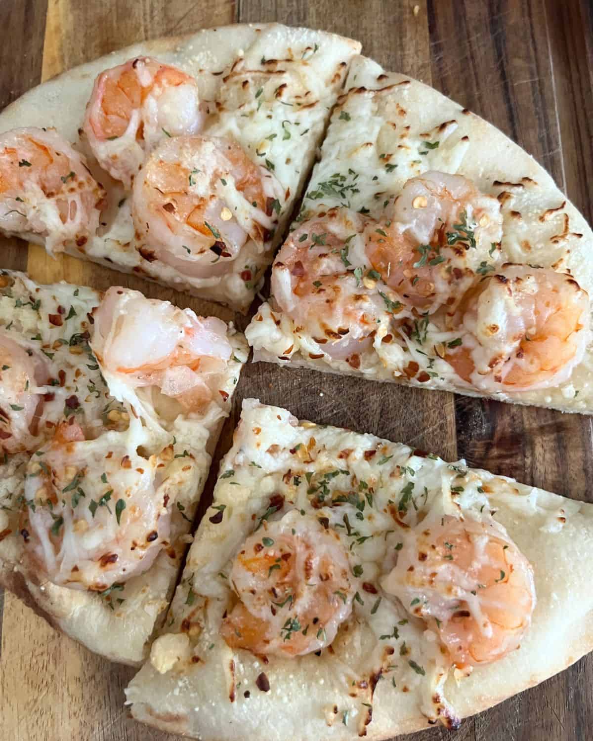 Grilled shrimp scampi flatbread pizza on a wooden cutting board. 