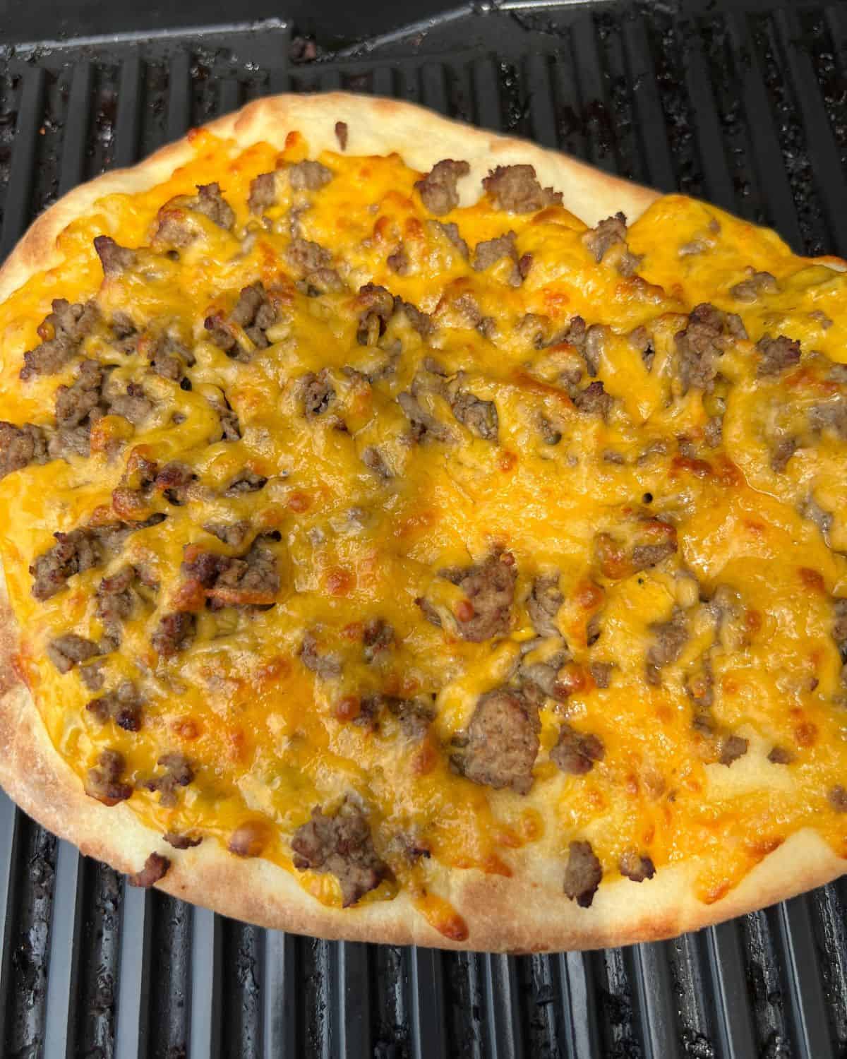 Naan bread topped with nacho cheese sauce and ground beef on a grill.  