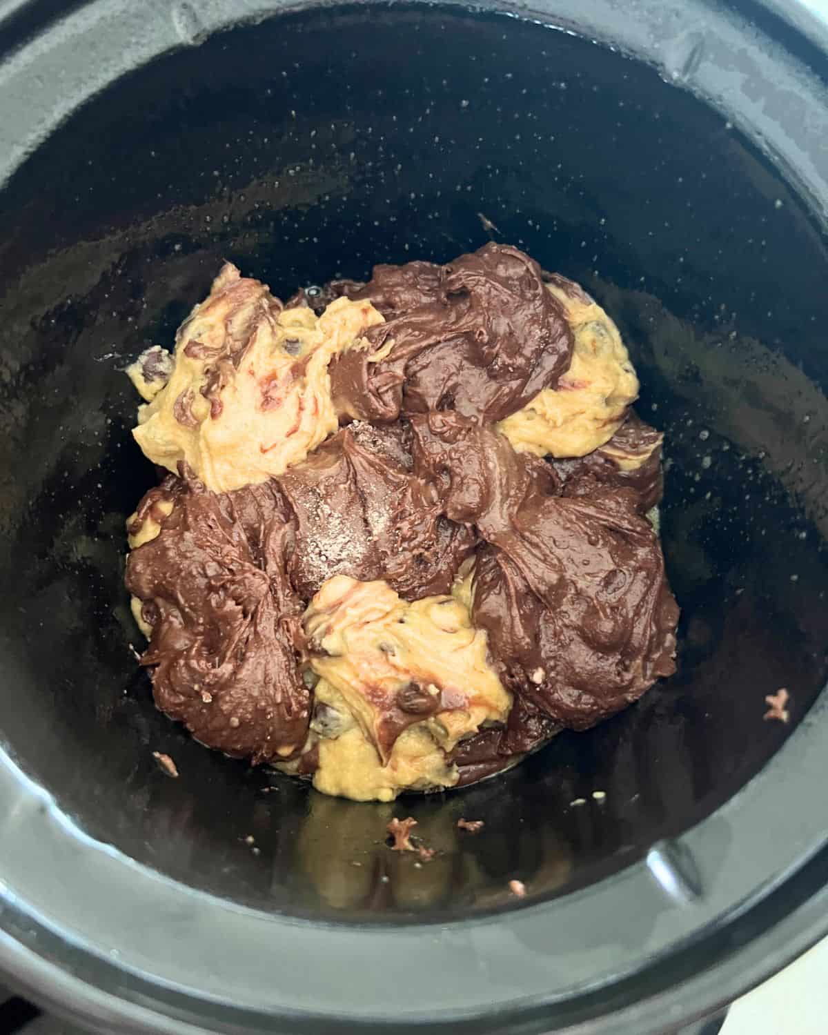 Alternating brownie batter and cookie dough batter together in a crock pot. 