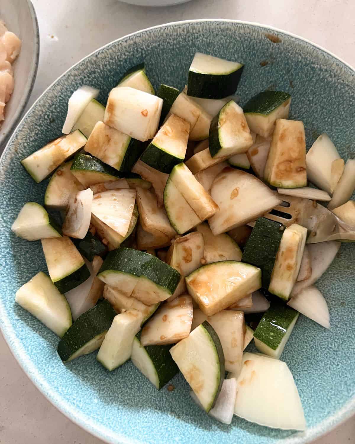 Zucchini and onions in a bowl with the sauce. 