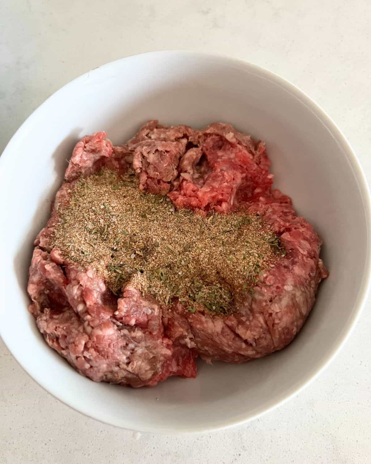 Mixed seasonings and garlic in a bowl with ground beef. 