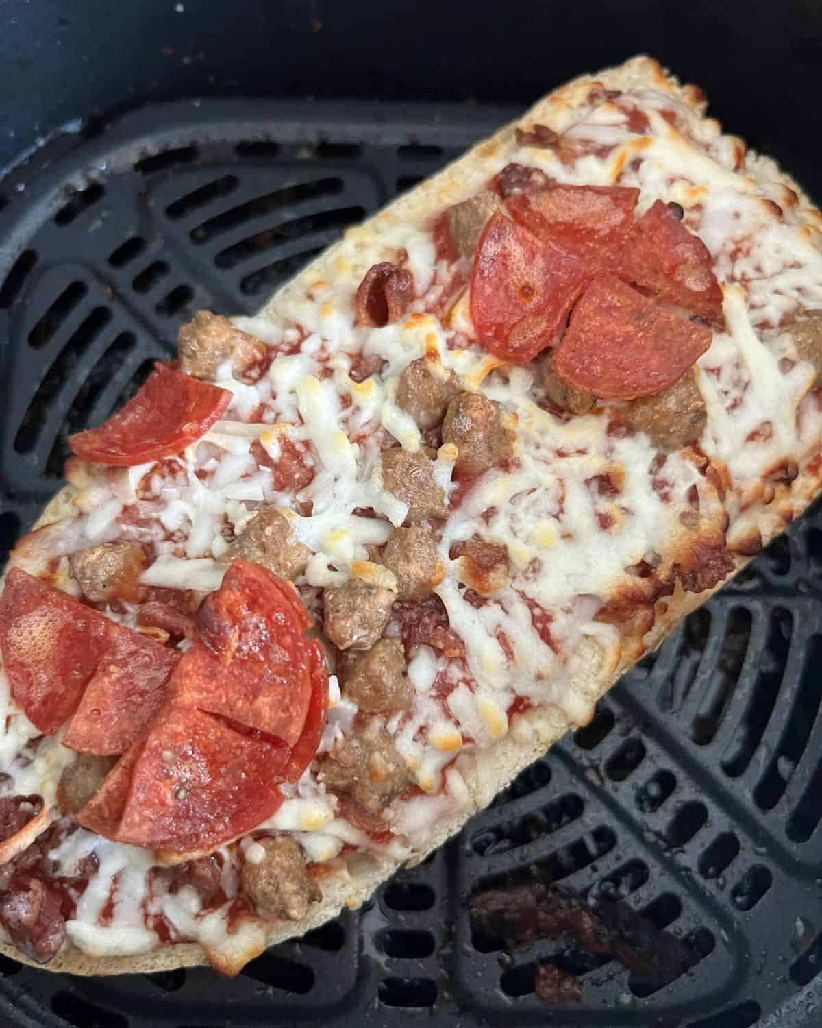 Finished air fried cooked pizza in air fryer basket. 