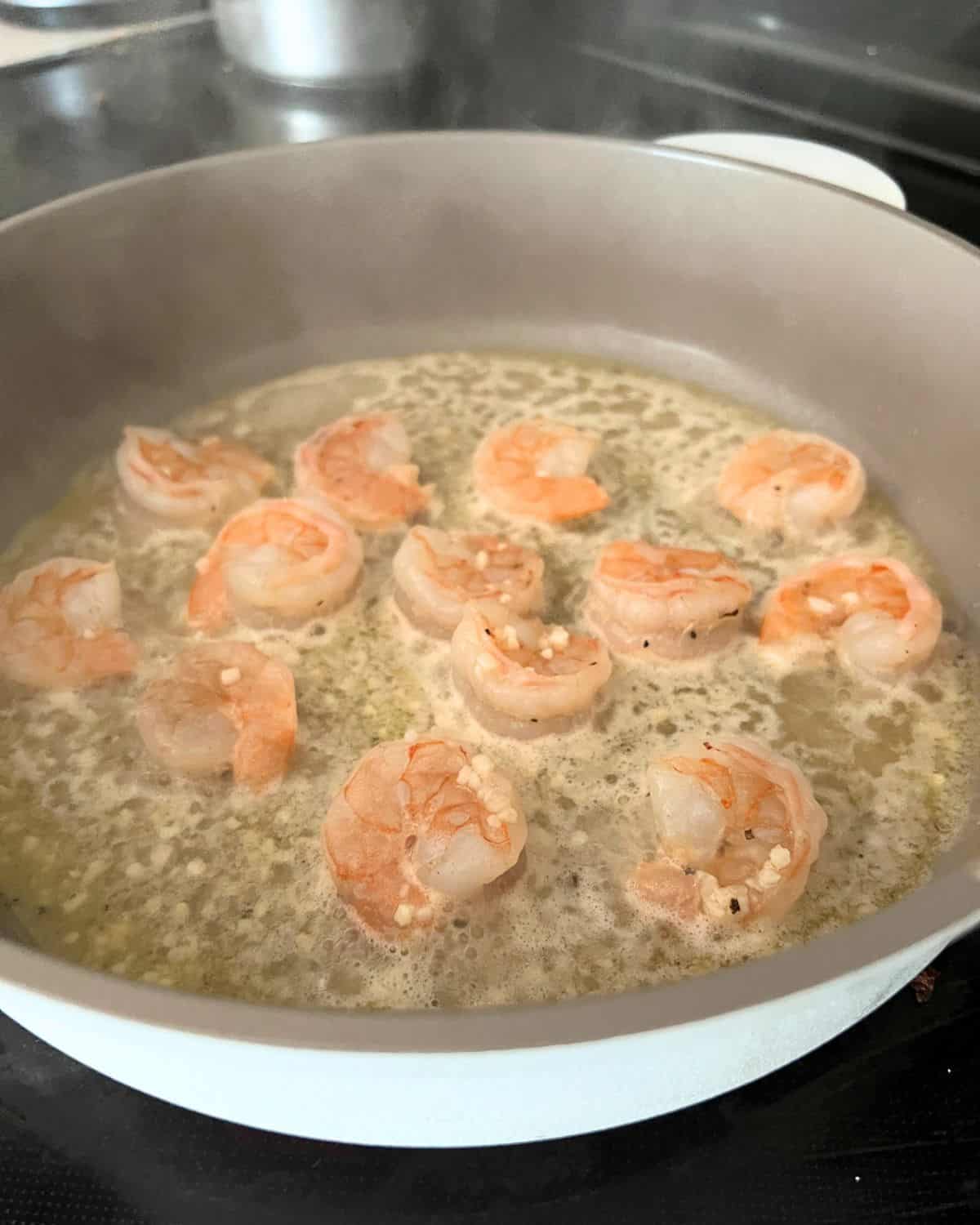 Shrimp cooking in a skillet with butter, garlic, and olive oil. 