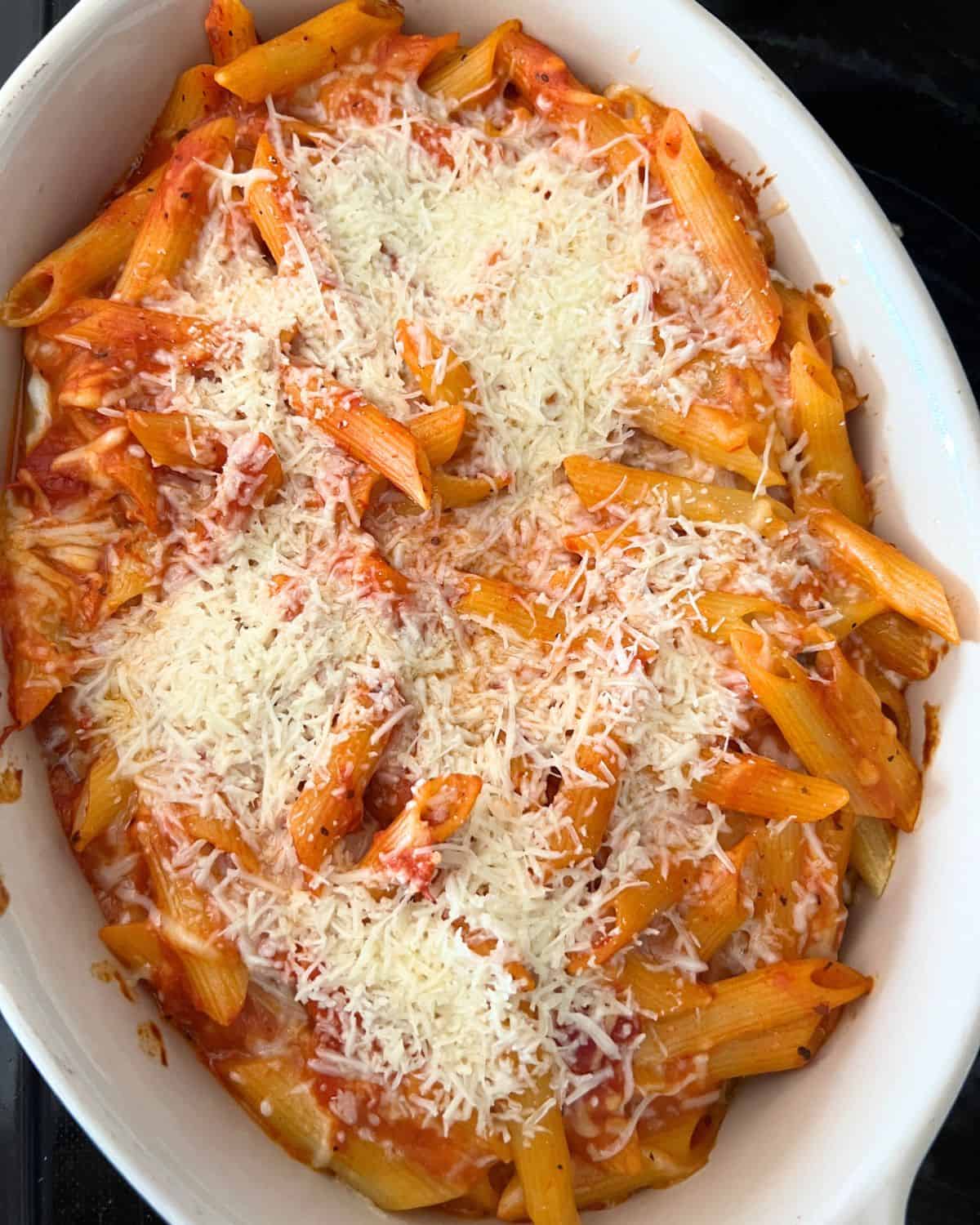 Noodles, cheese, and sauce in a baking dish topped with parmesan cheese. 