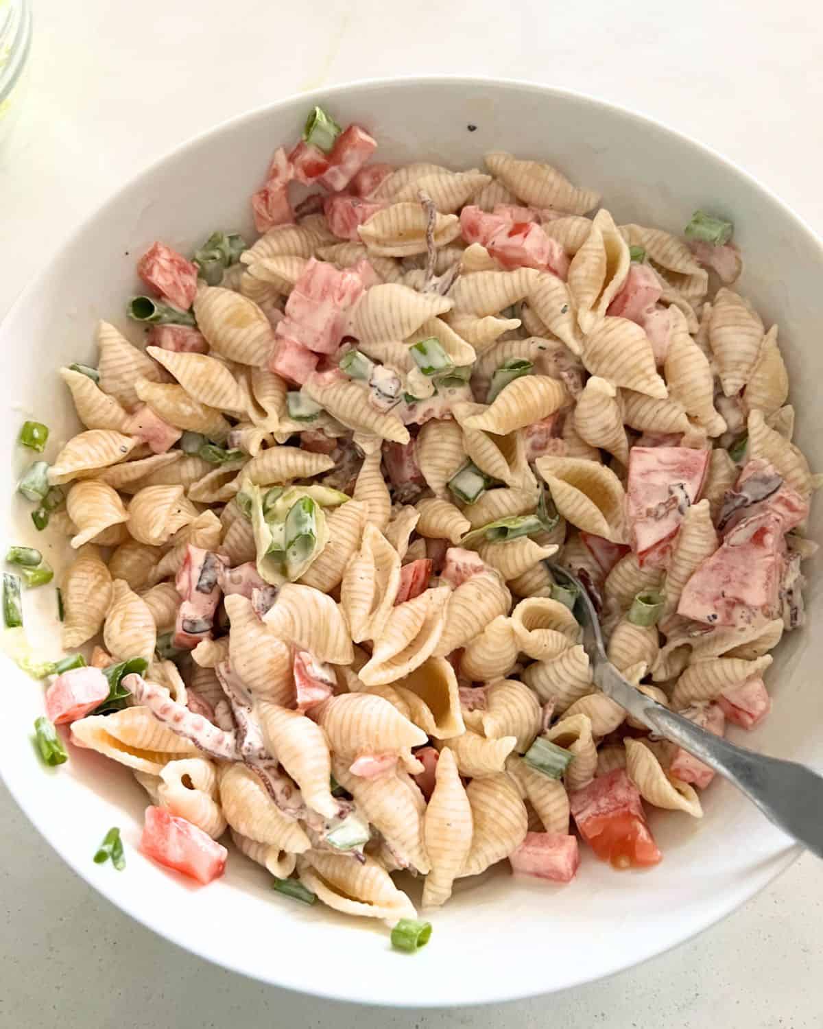 Dressing and pasta salad ingredients combined in a bowl. 