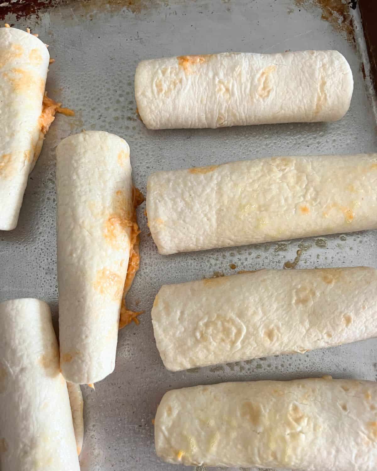 Buffalo Chicken Taquitos arranged on a baking sheet. 