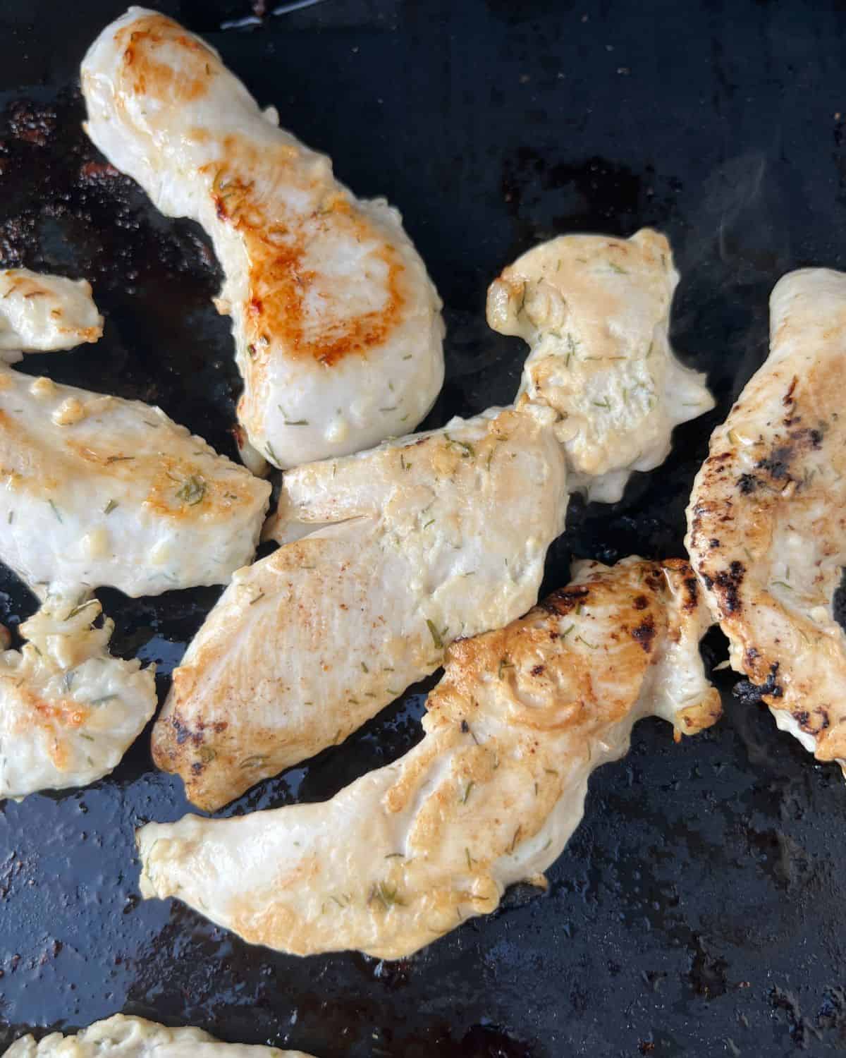 Chicken tenders cooking on a an outdoor griddle. 