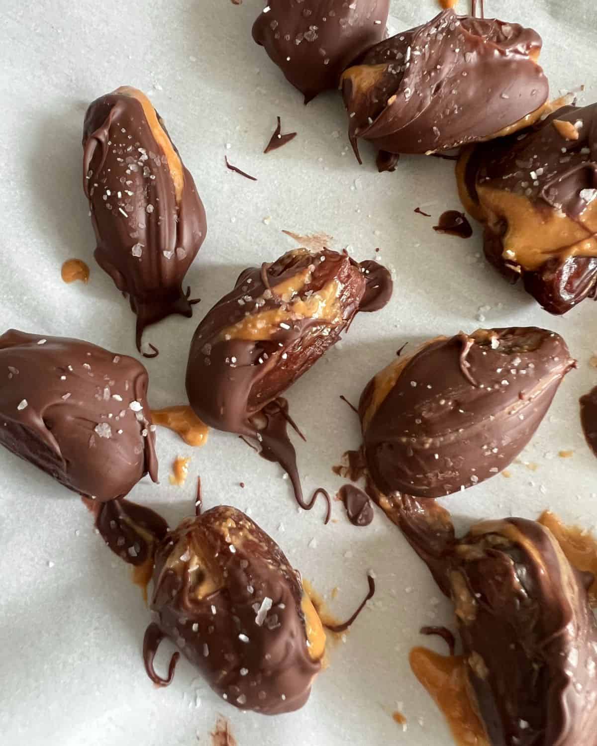 Peanut butter stuffed dates dipped in chocolate on parchment paper. 