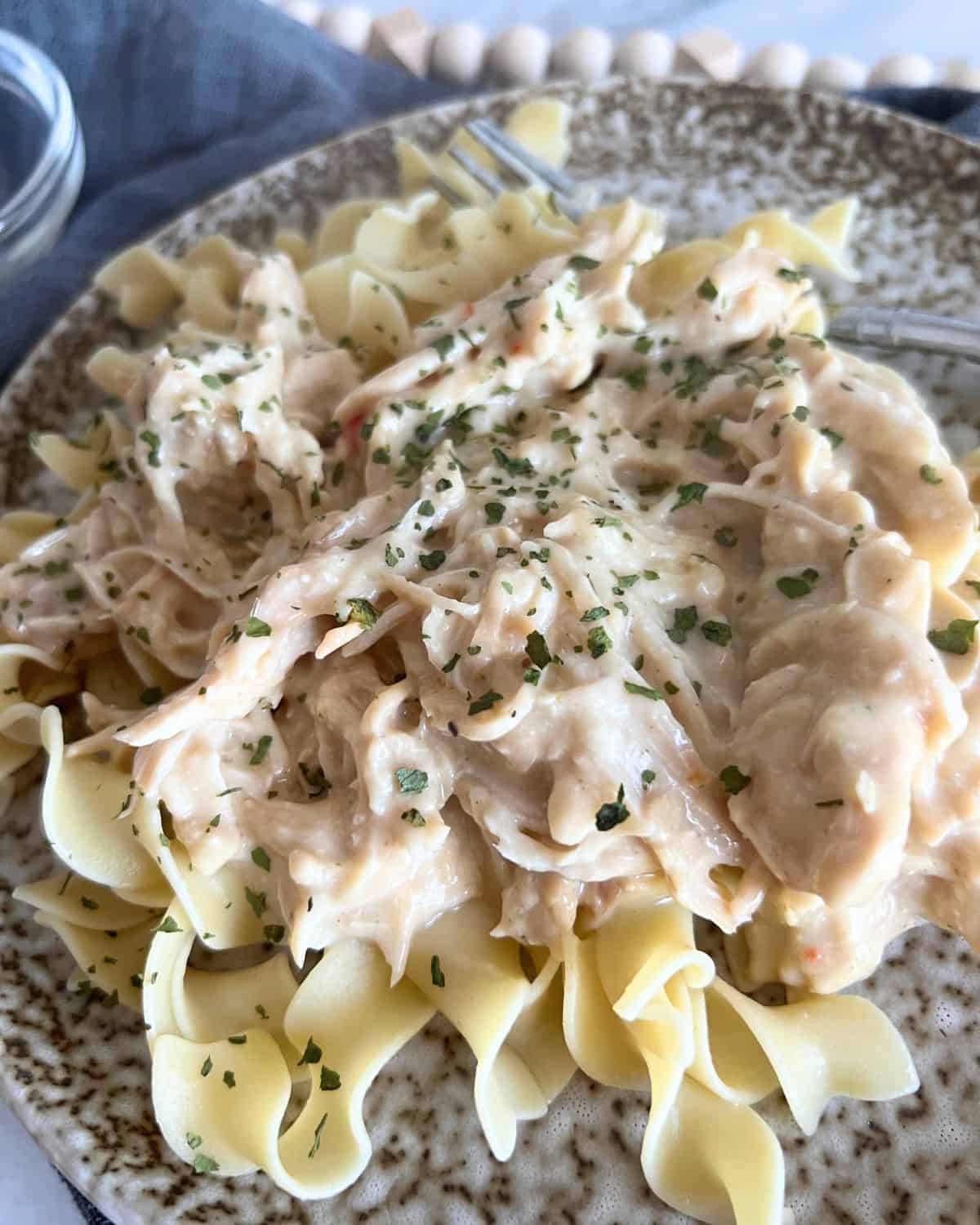 Crock Pot creamy Italian Chicken garnished with parsley flakes on a brown plate. 