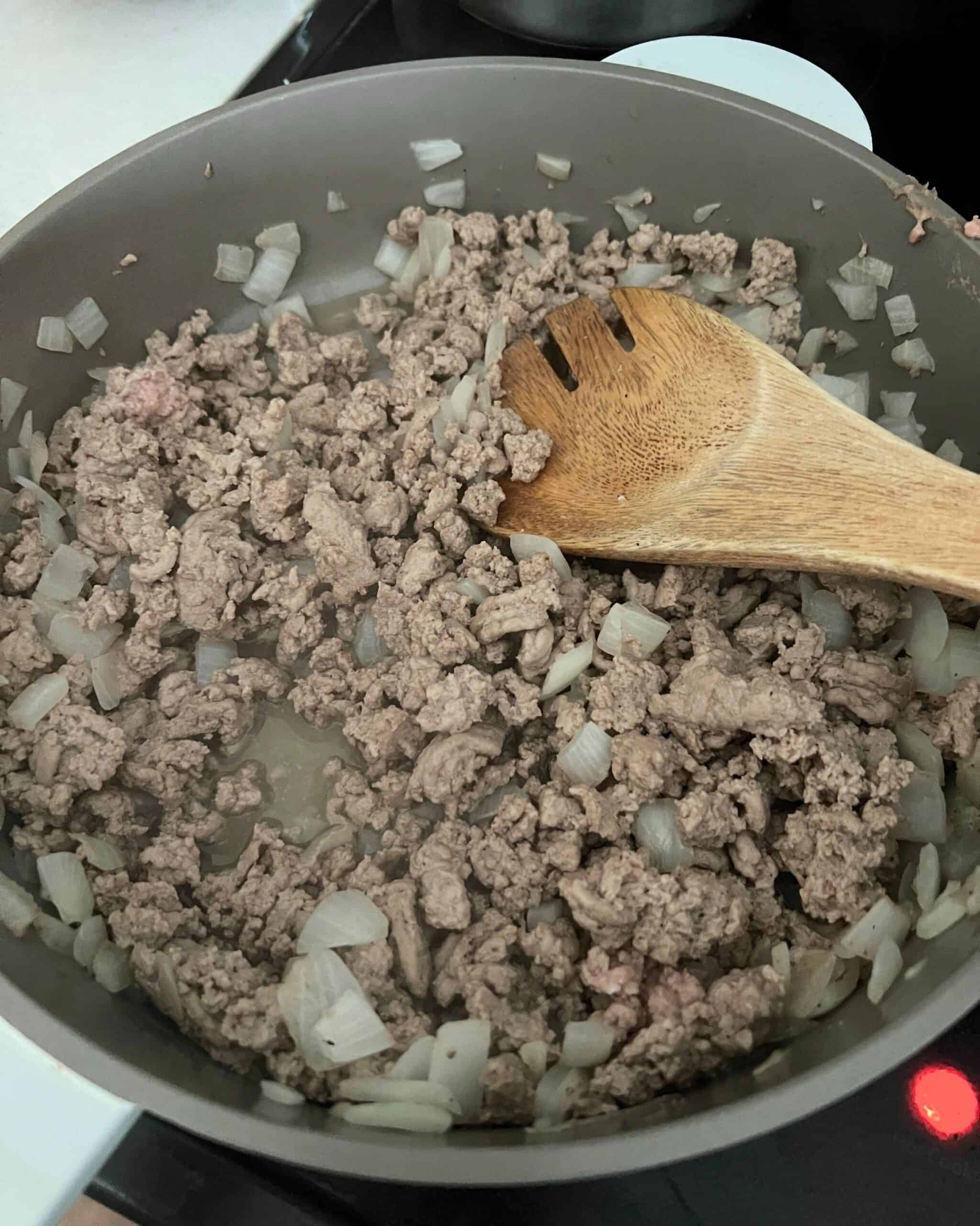 Ground turkey and onions cooking in a skillet with a wooden spoon. 