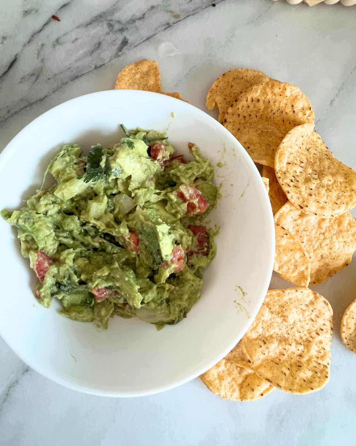 Guacamole in a white bowl next to chips. 