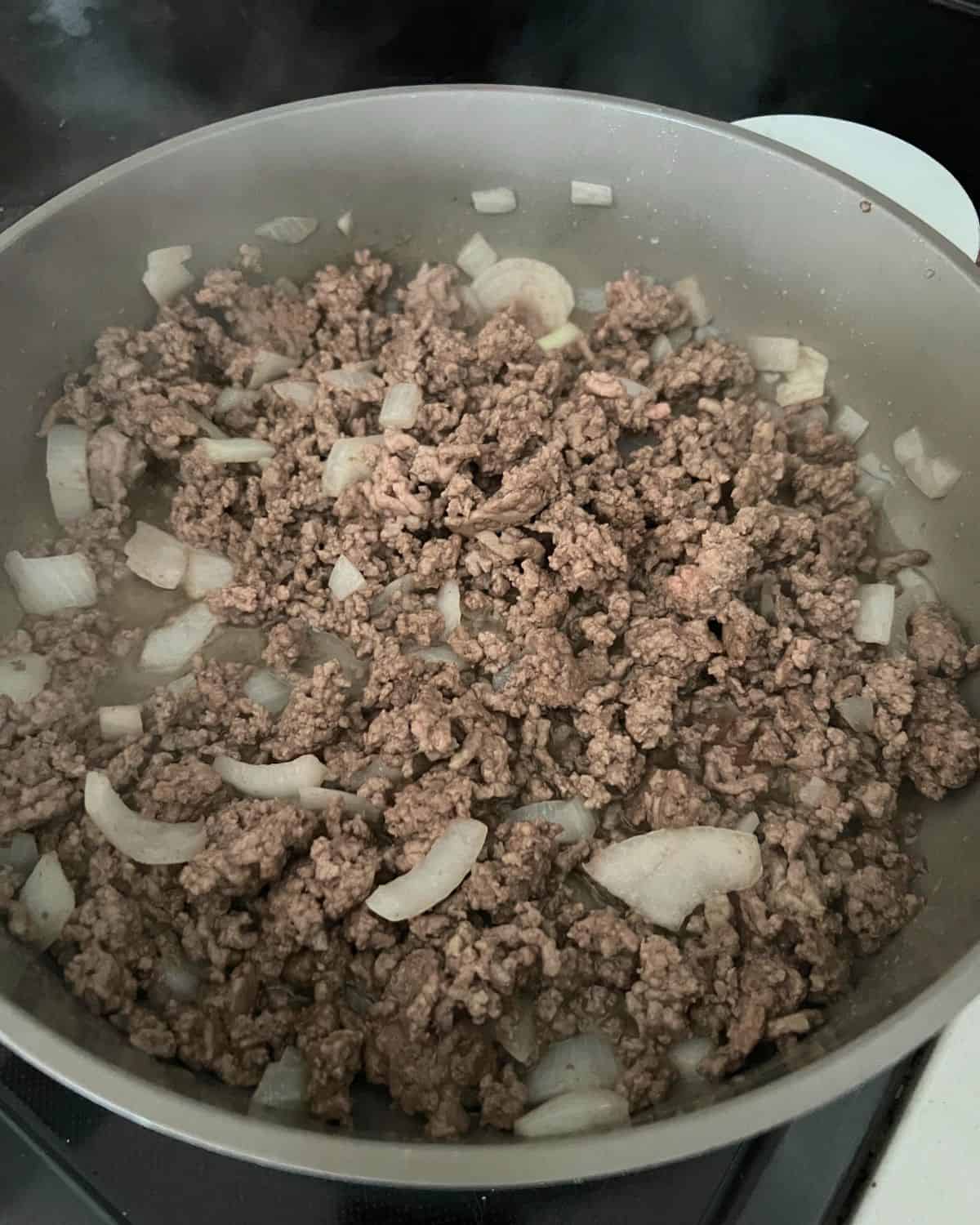 Onions and ground beef cooking in a skillet. 