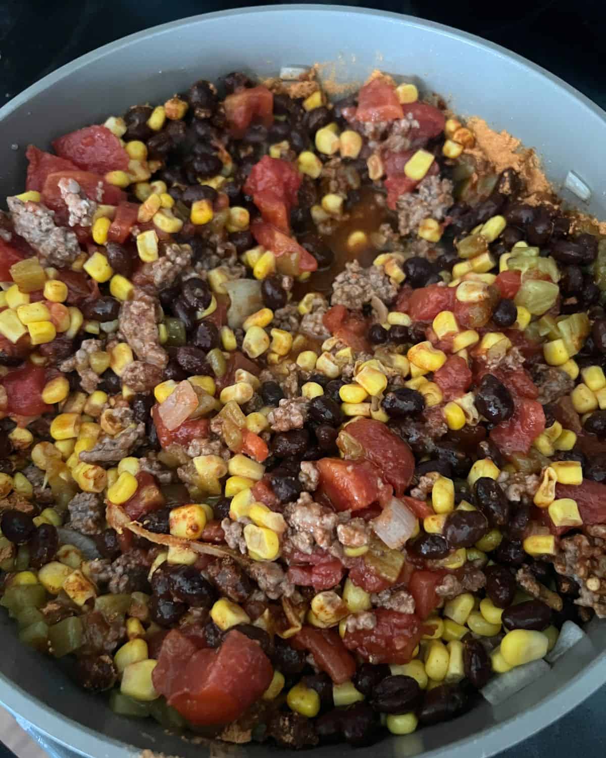 Corn, black beans, and tomatoes with ground beef cooking in a skillet. 