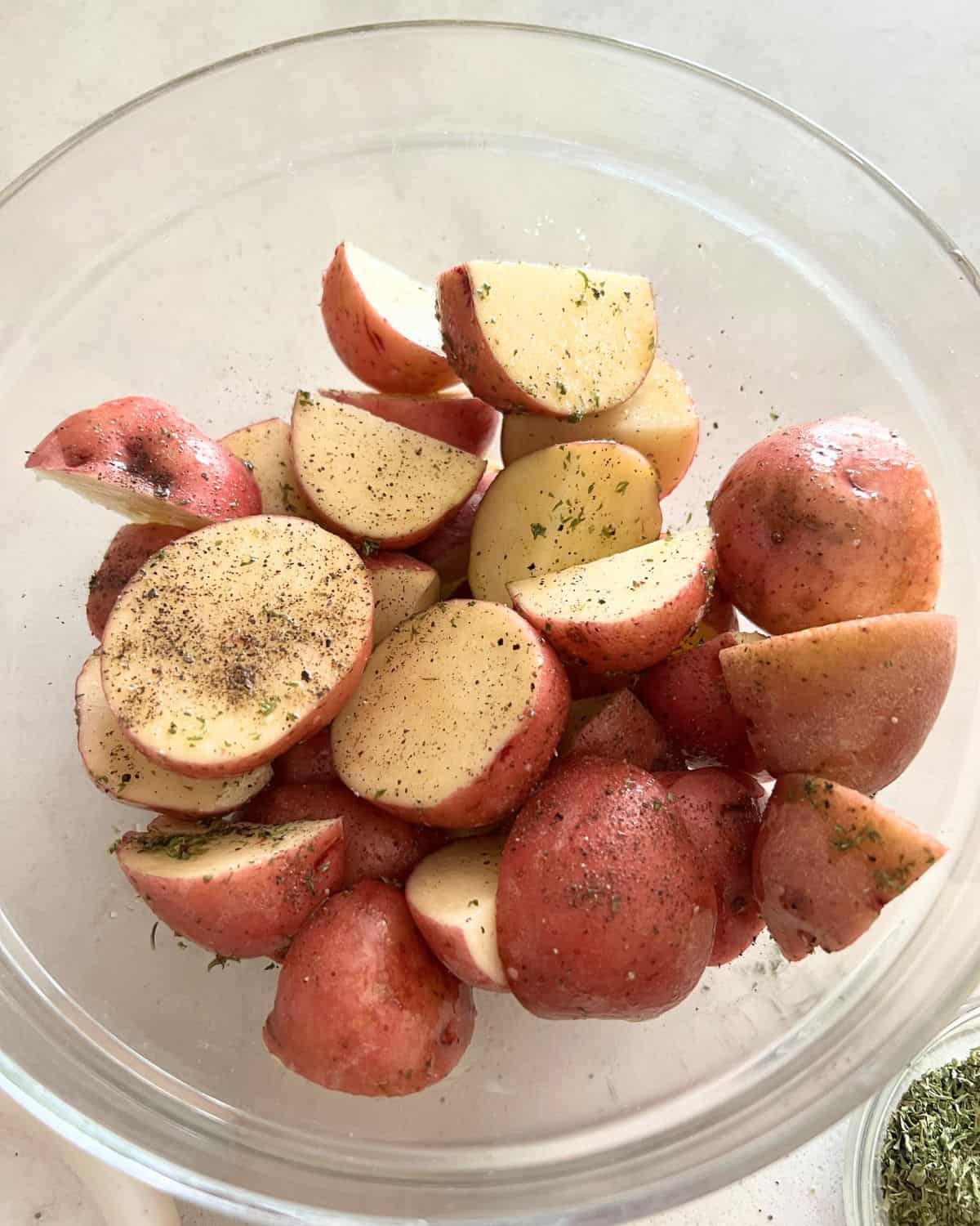 Potatoes and seasonings mixed together in a bowl. 