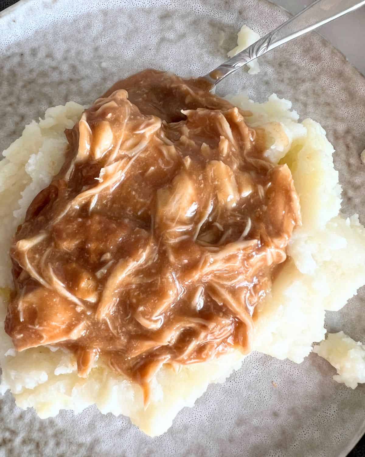 Chicken and gravy on top of mashed potatoes on a plate. 
