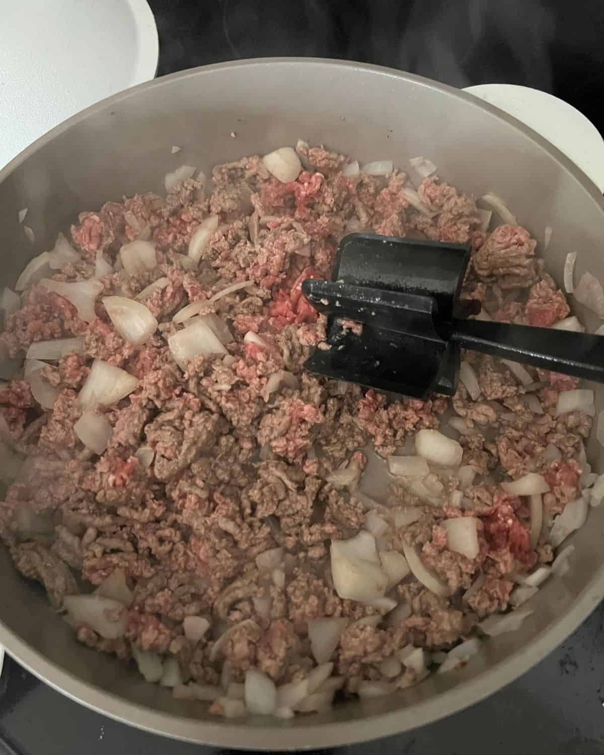 Onions and ground beef cooking in a skillet. 