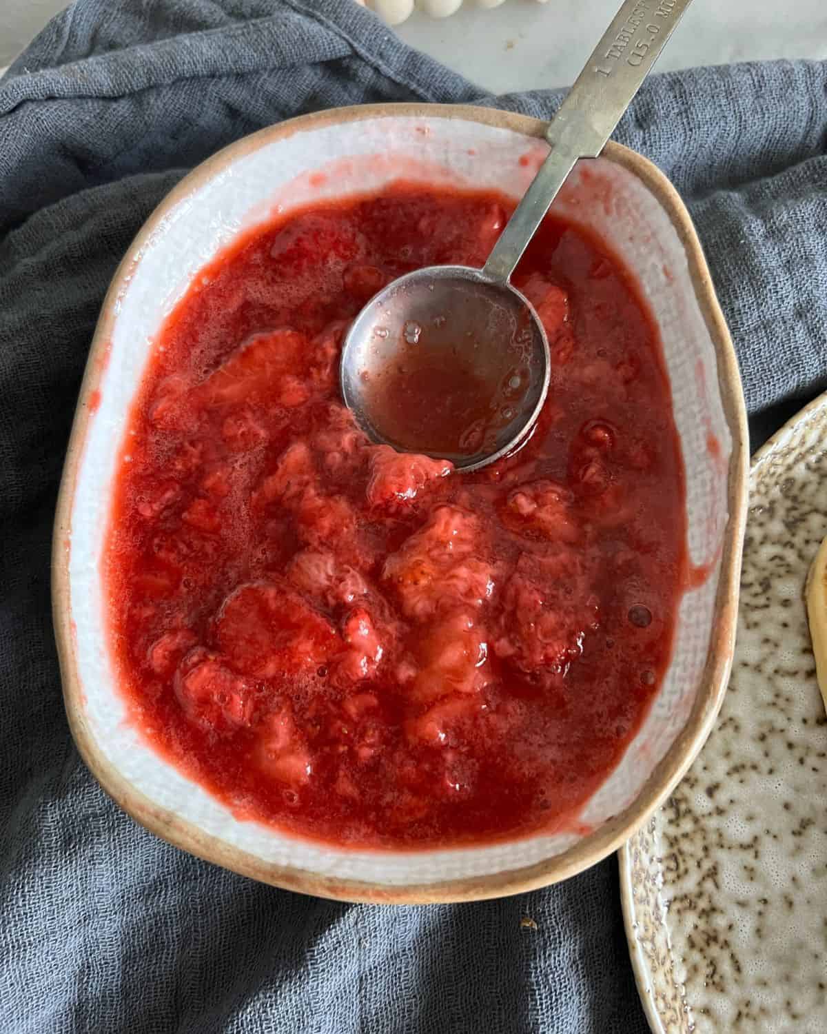 Sugar free strawberry sauce in a white serving dish with a spoon.