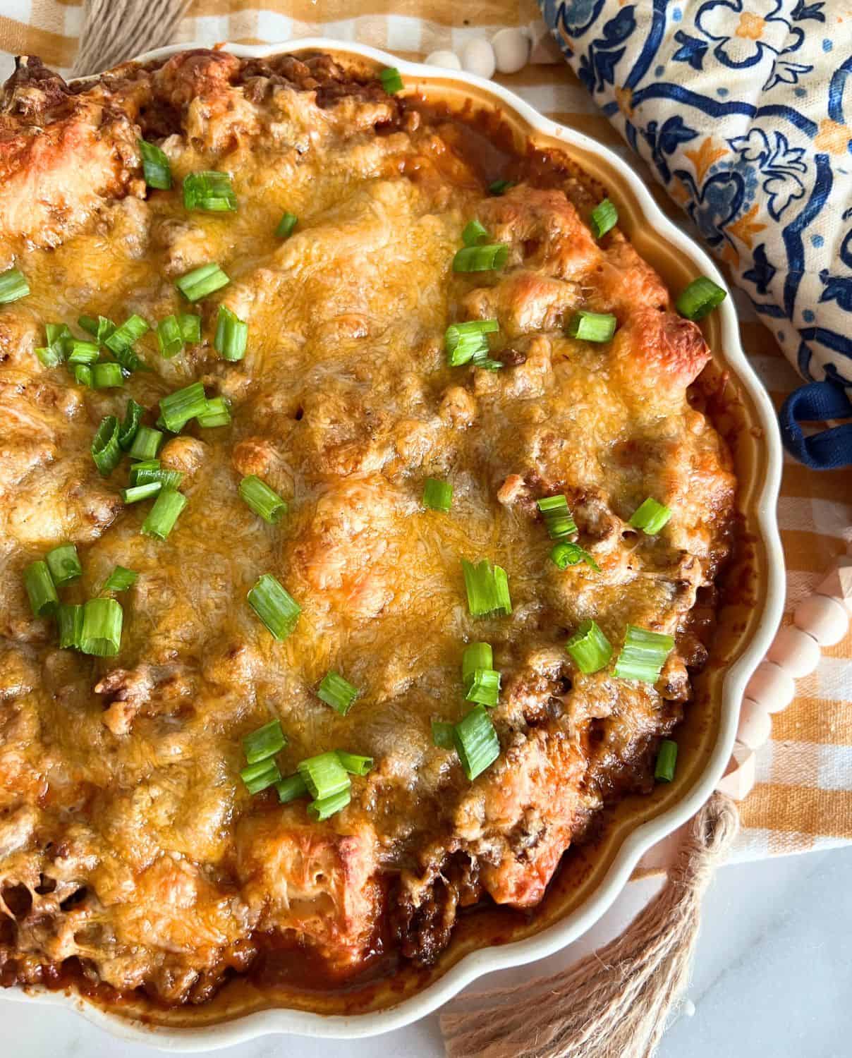 Bubble up enchiladas topped with green onions in a casserole dish. 