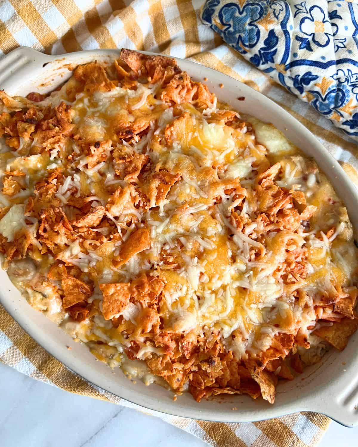 Chicken Dorito casserole topped with doritos and cheese in a white casserole dish. 