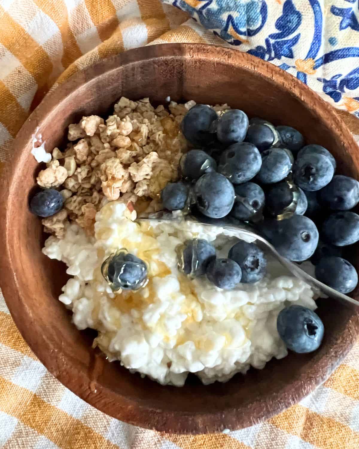 Cottage cheese breakfast bowl in a brown bowl topped with honey and fresh blueberries. 