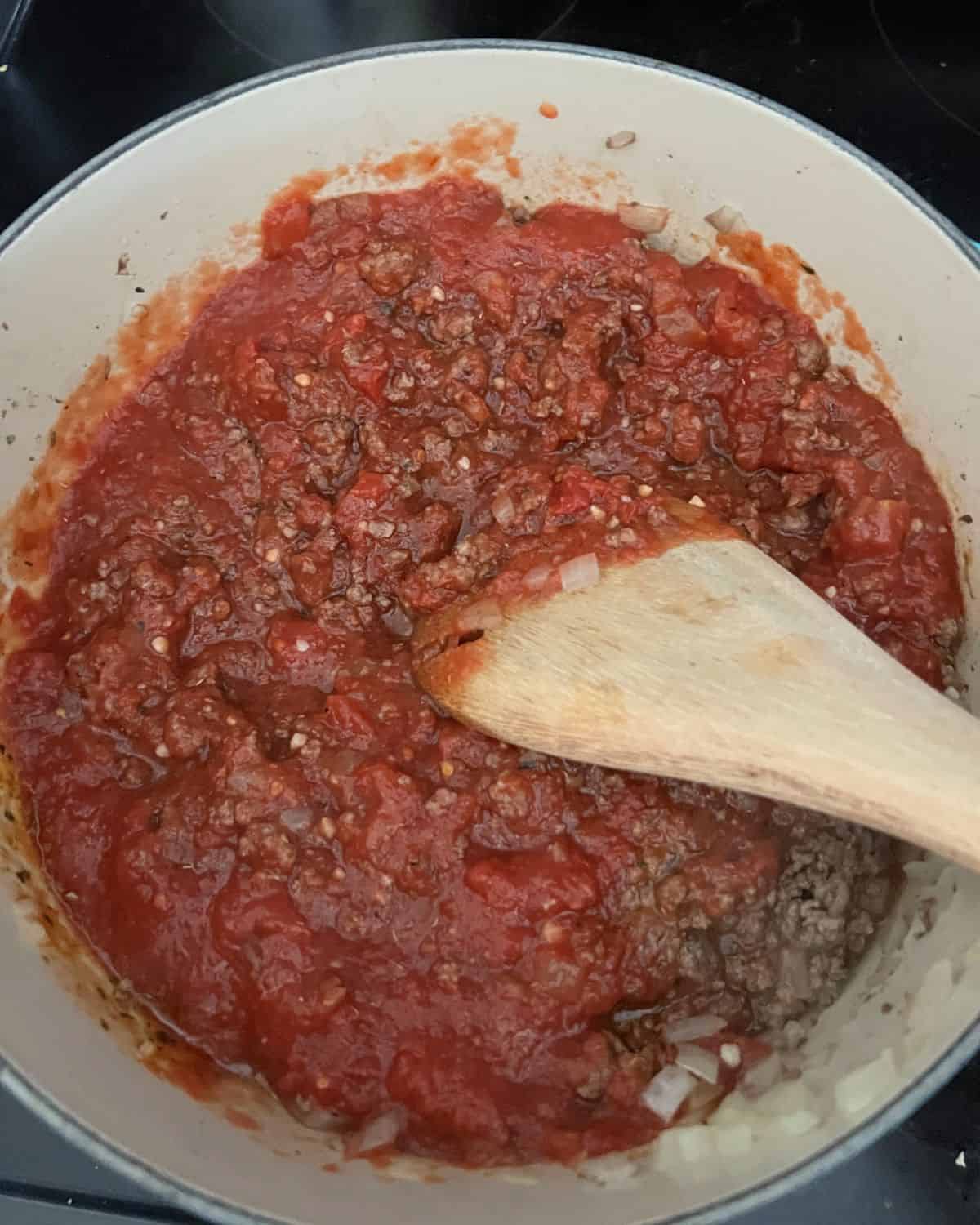 Crushed tomatoes over ground beef and onions in pot. 