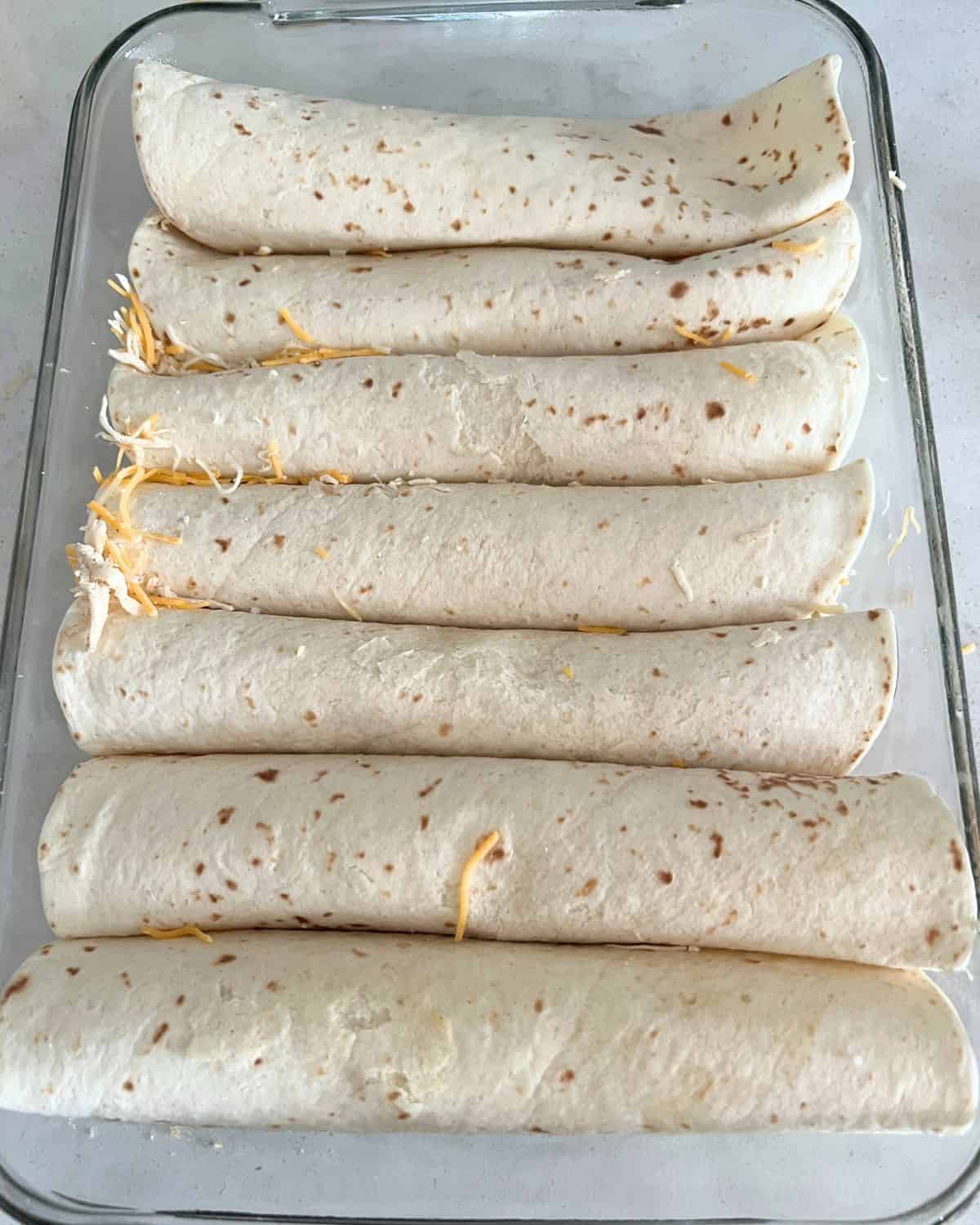 Chicken rolled up into tortillas in a casserole dish. 
