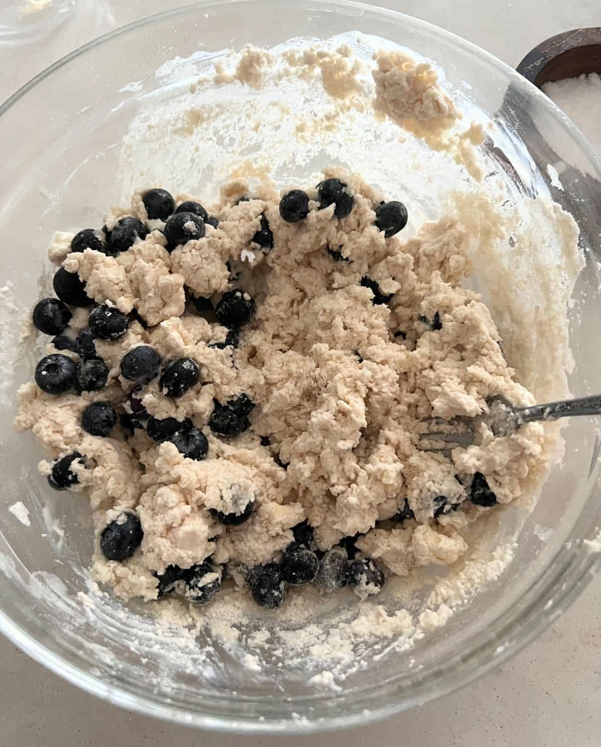 Blueberries and buttermilk mixed with dry ingredients in a bowl. 