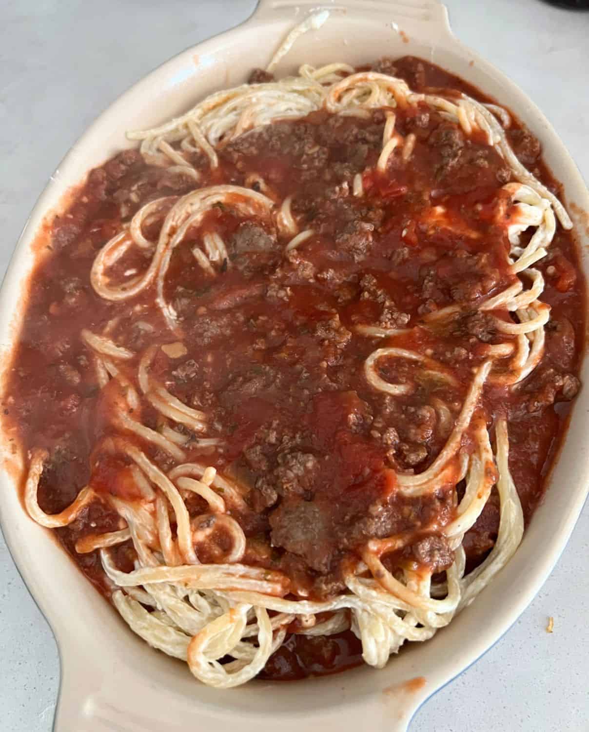 Layered noodles and meat sauce in a casserole dish ready for the oven. 