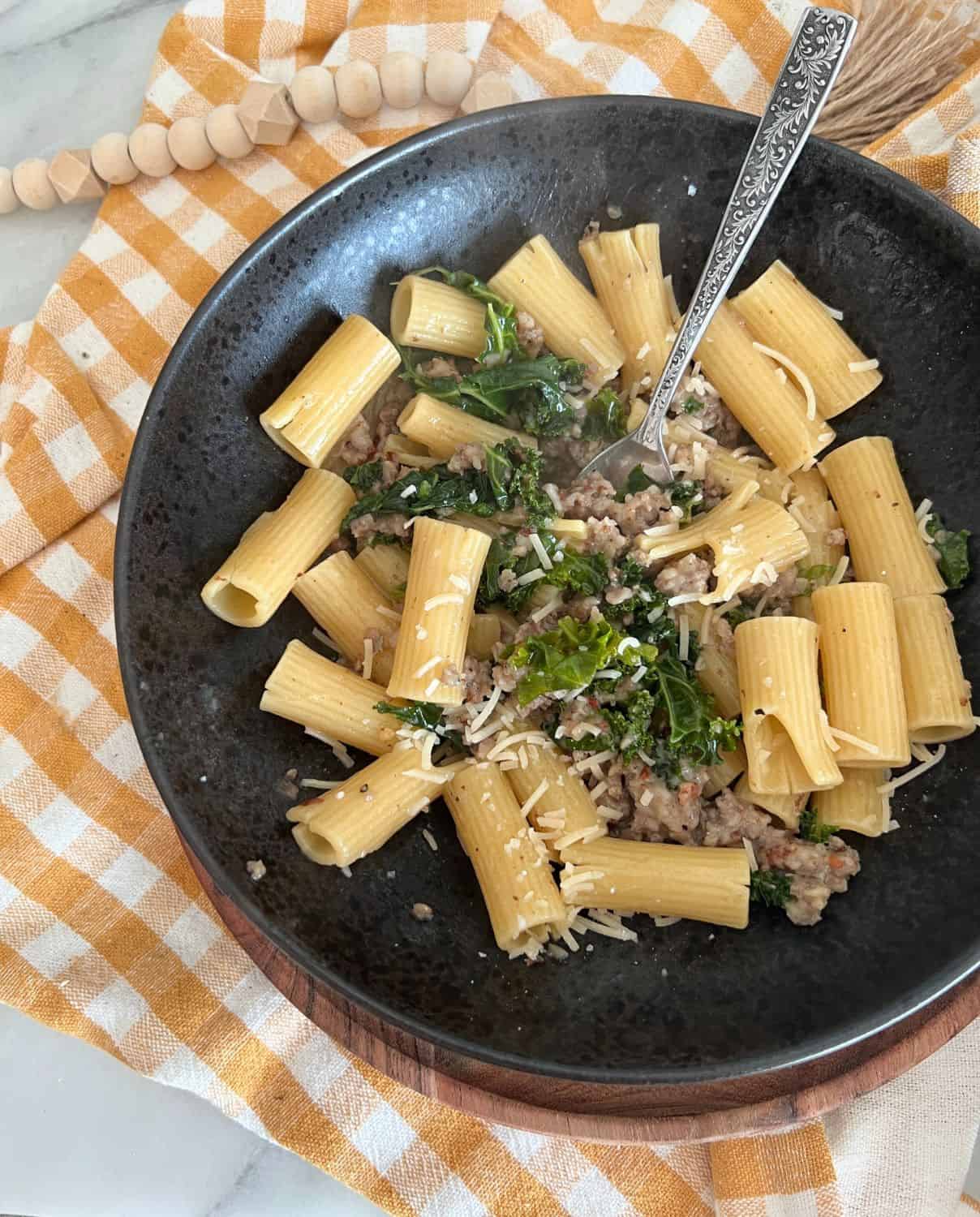 Finished rigatoni with sausage and kale in a black bowl with a fork. 