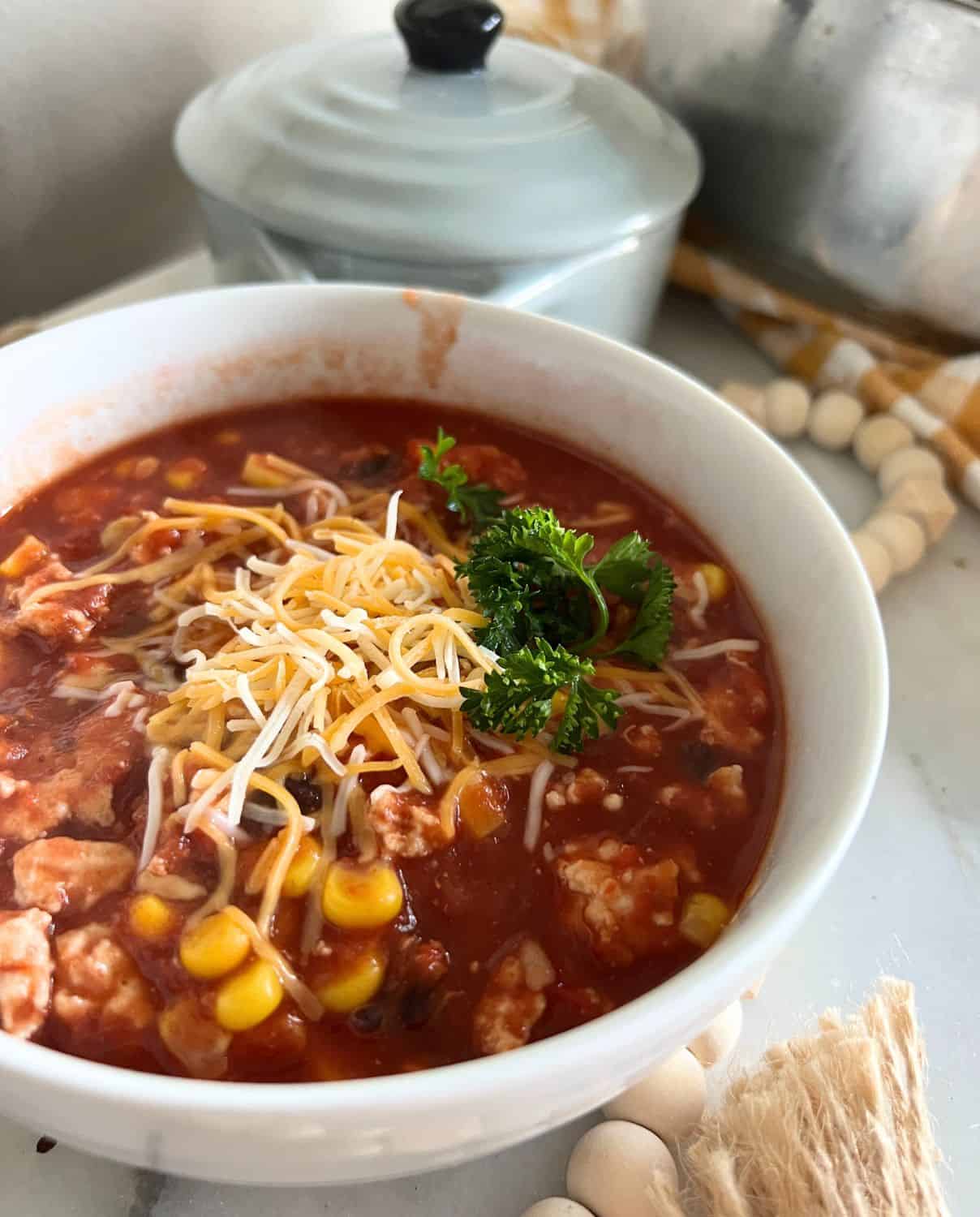 Turkey, Corn, and Black Bean Chili topped with cheese and fresh parsley in a white bowl. 