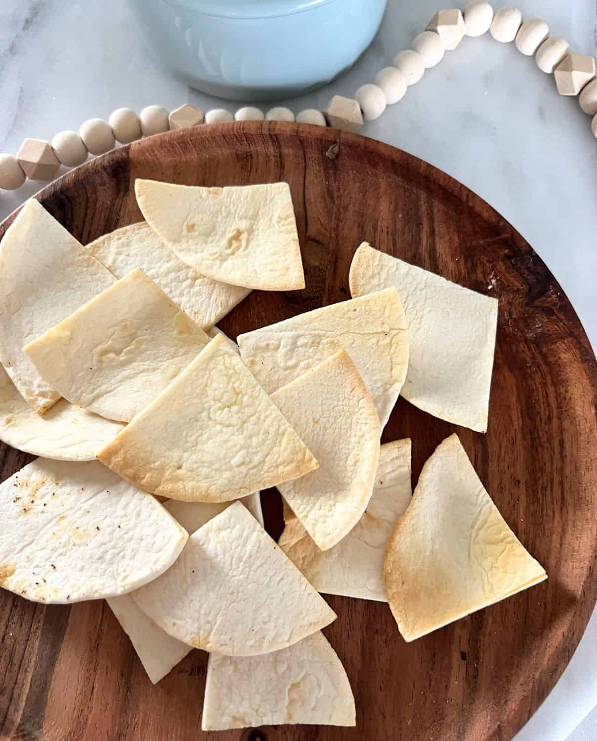 Air fryer tortilla chips on top of a wooden serving plate. 